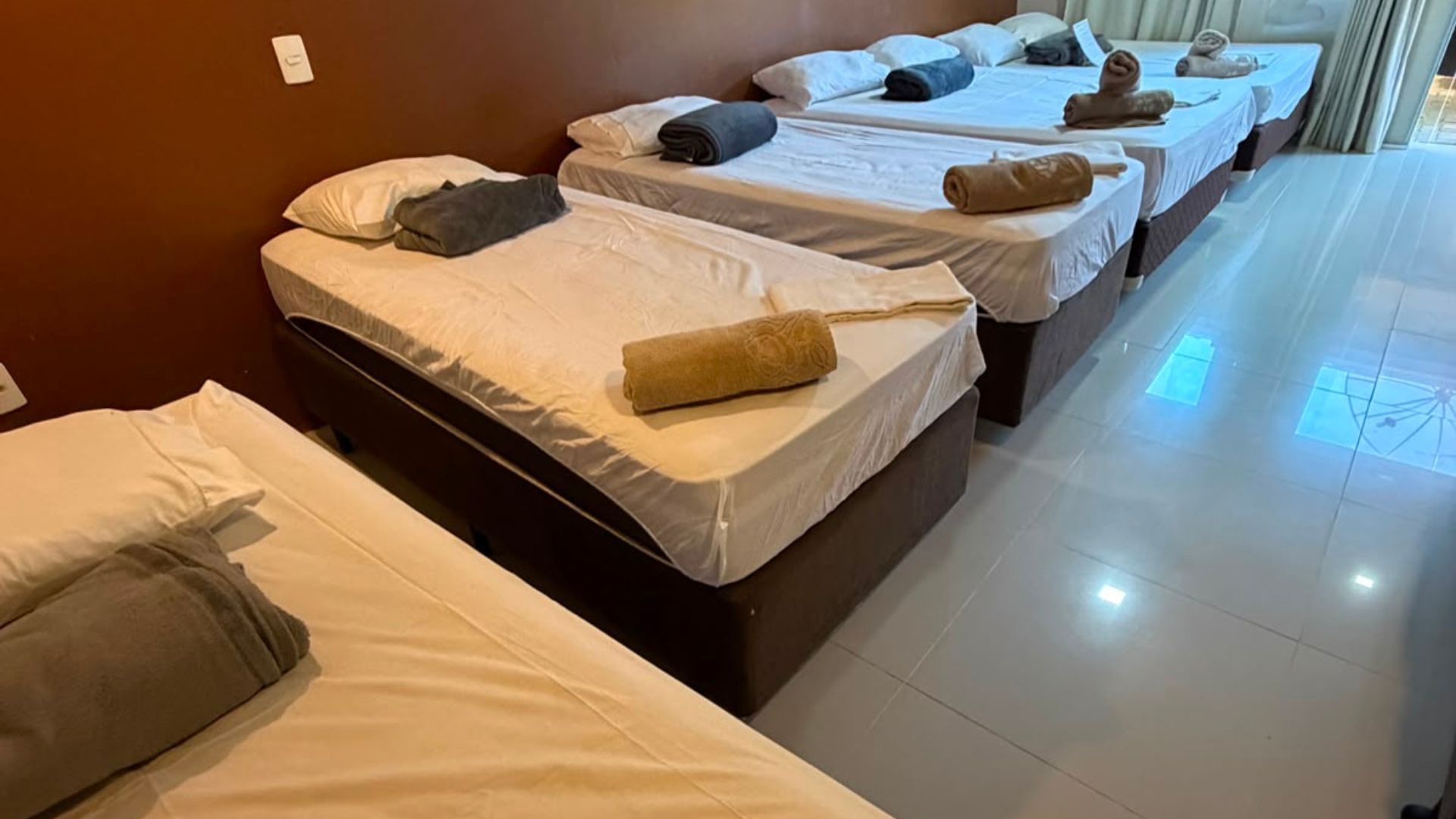 Fileira de camas de solteiro arrumadas em um quarto iluminado estilo dormitório, com toalhas e travesseiros.