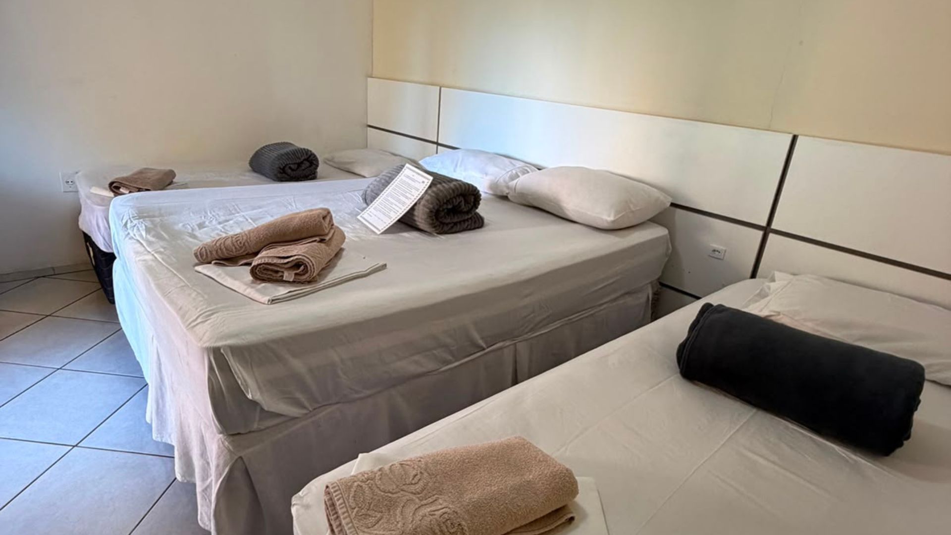 Duas camas de solteiro arrumadas com toalhas dobradas em um quarto de hotel simples e luminoso.