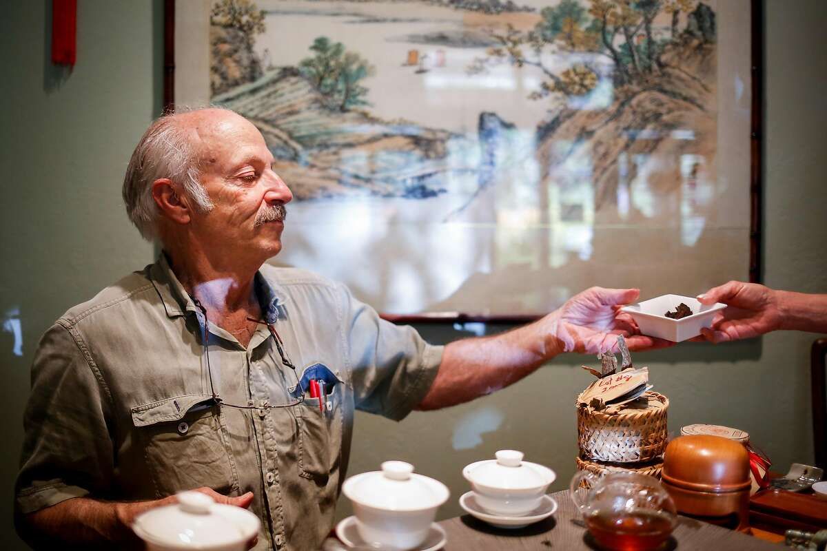 Man reaching out to receive a small cup at a tea table with teapots and a painted wall mural