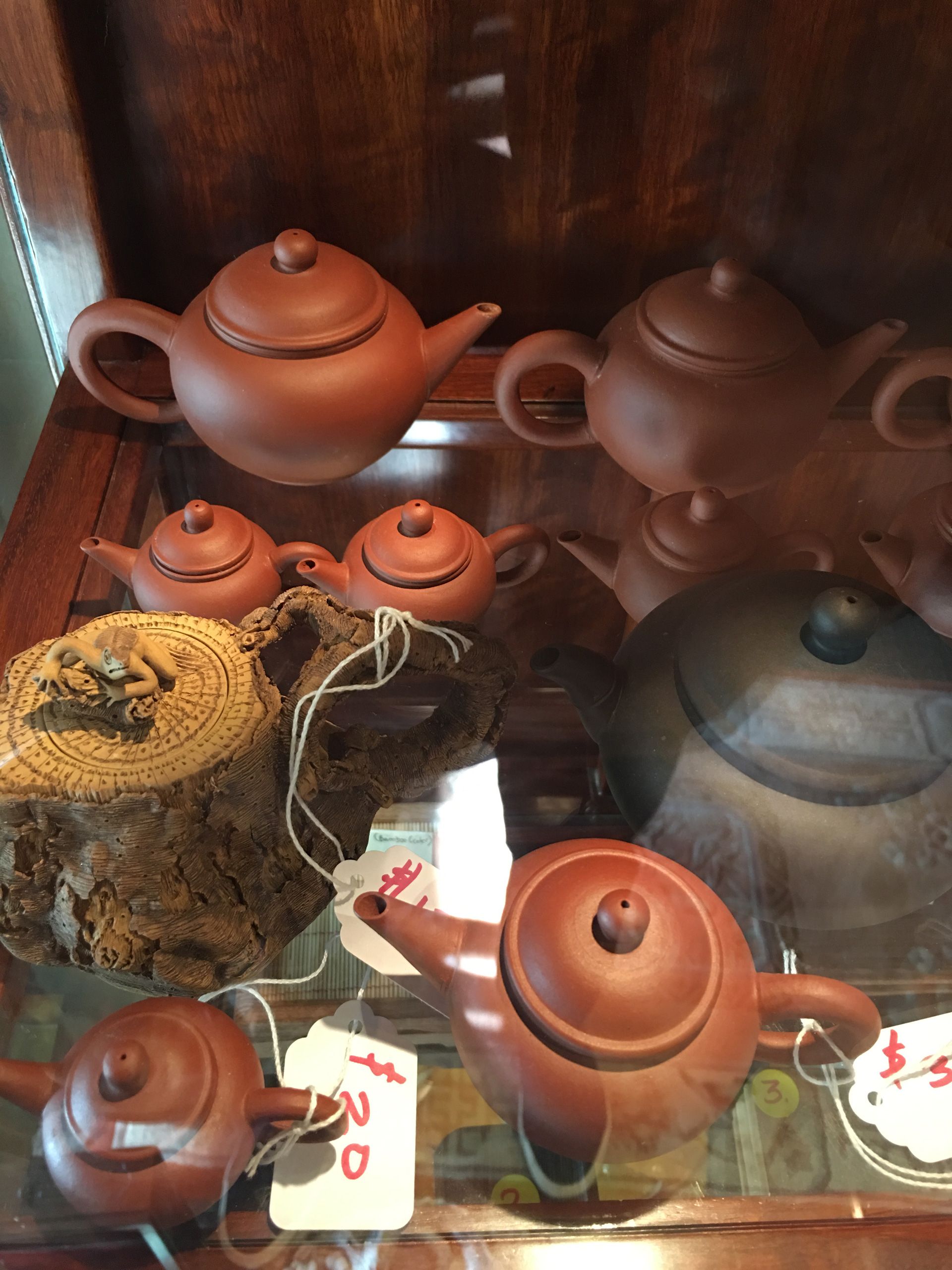 Assorted clay teapots on display in a glass cabinet, mostly brown and orange.