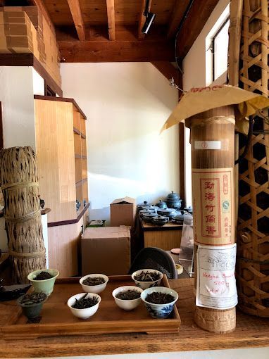 Traditional room with wooden ceiling, rice bowls on the floor, and a tall decorated ceremonial pillar.