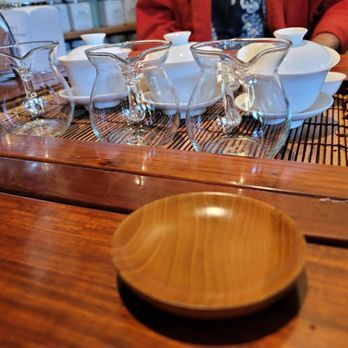 Wooden table with a small bowl in the foreground and stacked glass cups and bowls behind it at a café counter