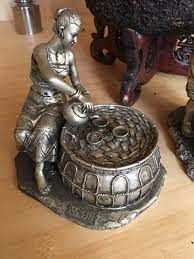 Small bronze figurine of a person leaning over a coin-filled well on a wooden table