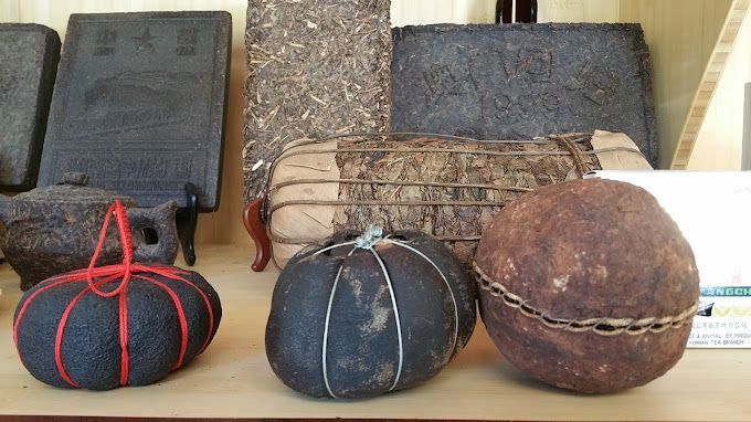 Three wrapped, round bundles sit on a shelf in front of woven baskets and black cases.