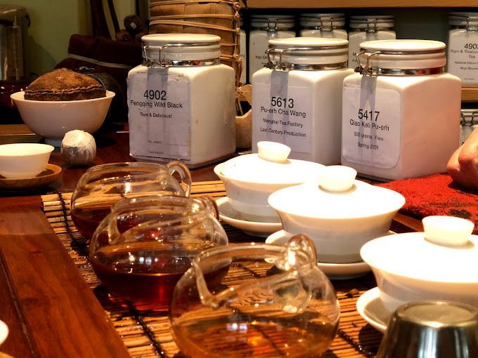 Tea tins and white teacups on a wooden table, with glass pots and a bowl of tea leaves.