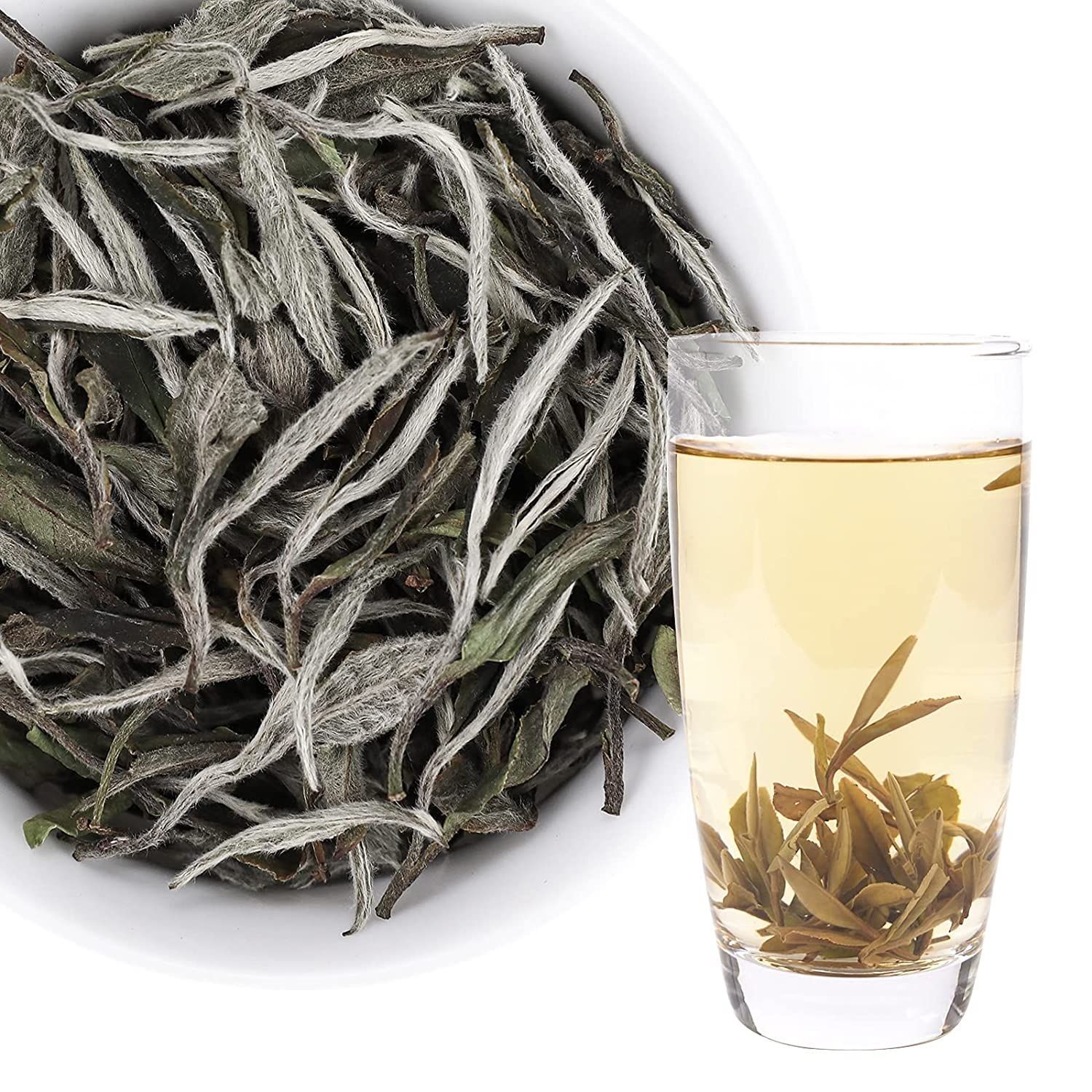 Loose tea leaves beside a glass of pale tea with leaves floating inside