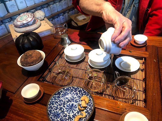 Person pours tea into white cups on a wooden table with a blue patterned plate and snacks
