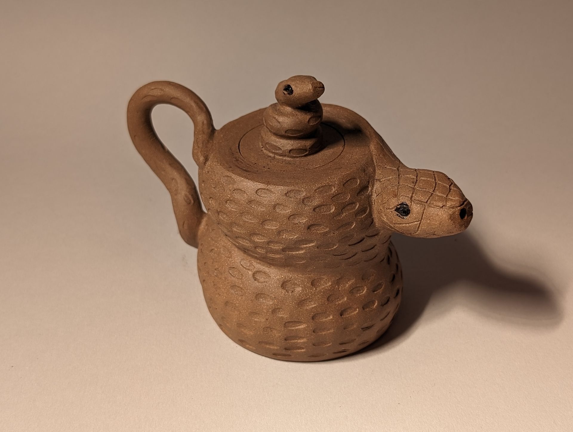 A brown teapot with a snake on top of it