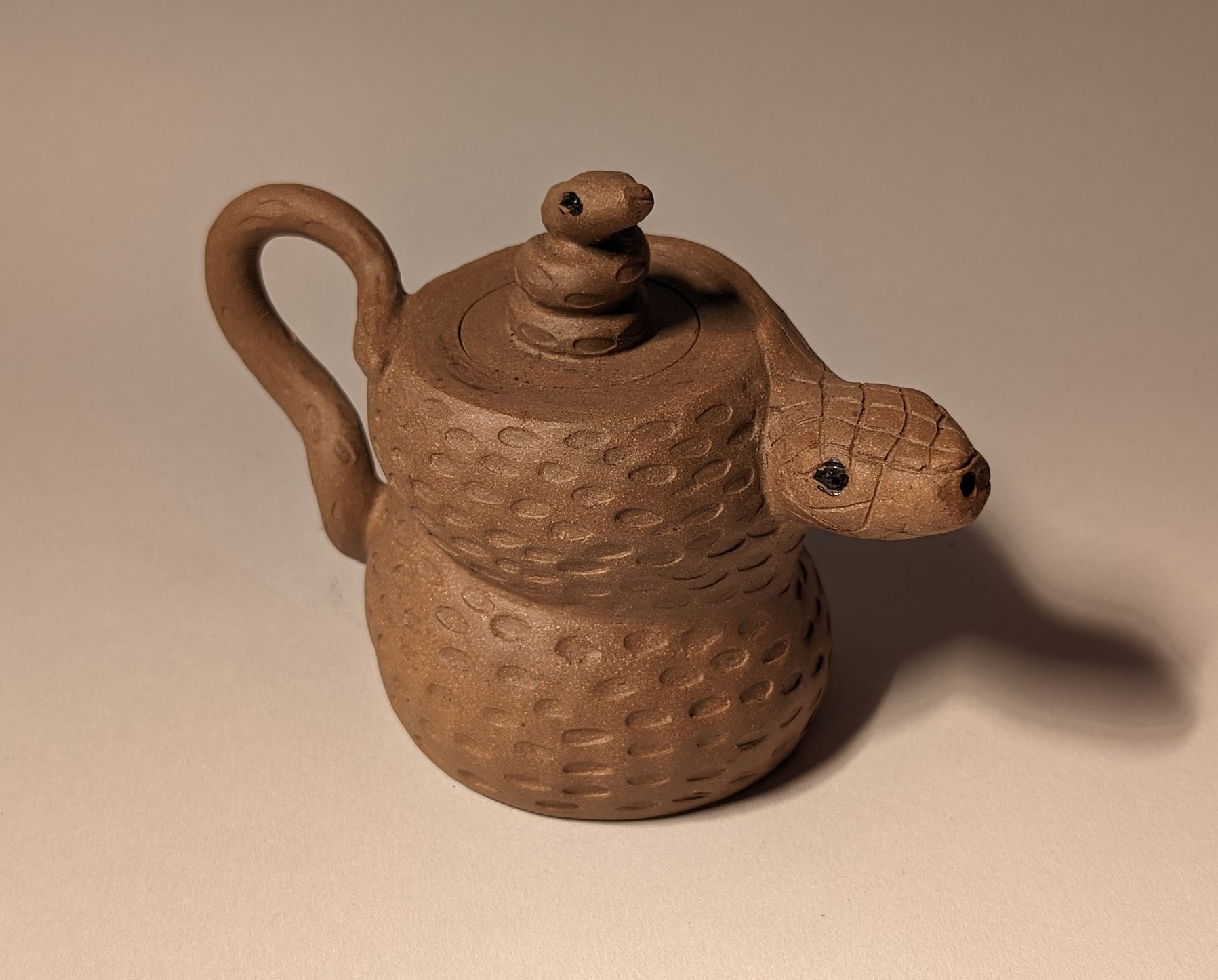 Small brown ceramic teapot shaped like a coiled snake with a lid and spout.