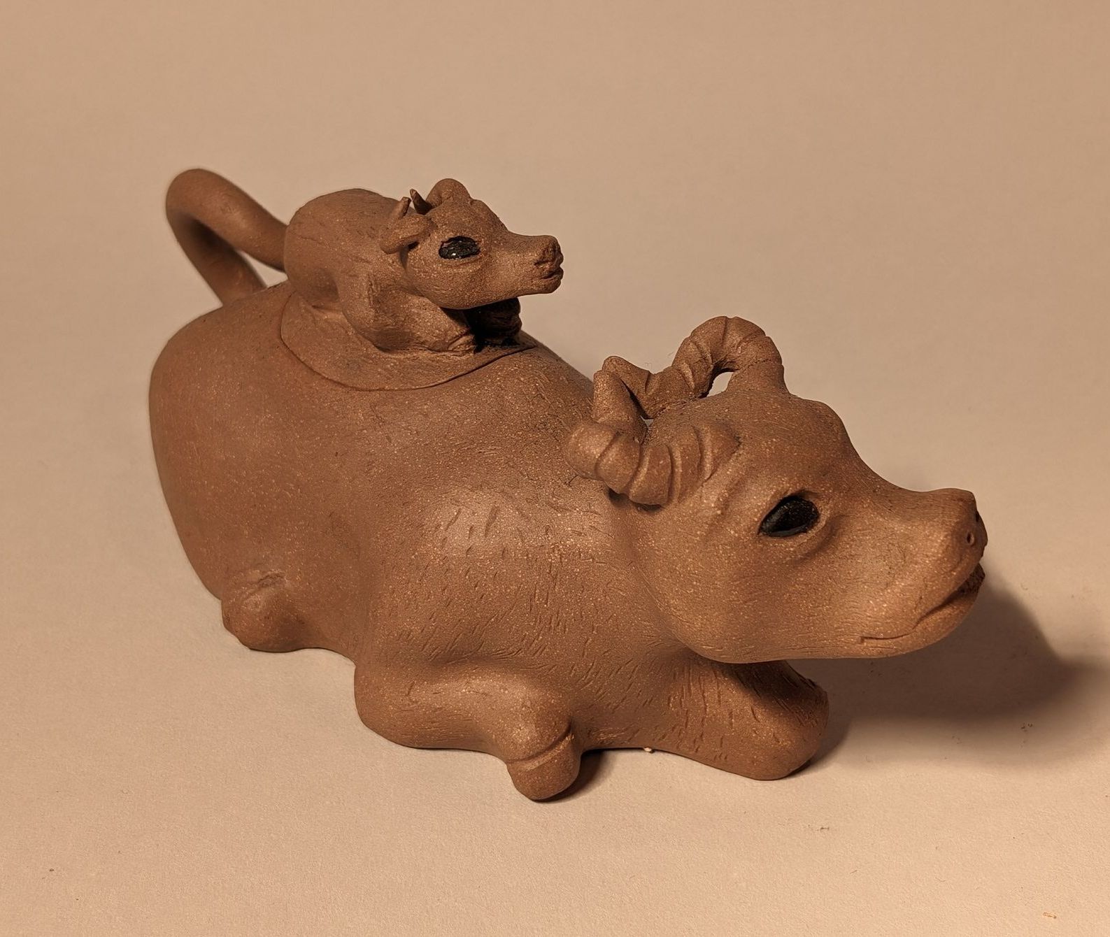 Small brown figurine of a pig with a tiny animal riding on its back, on a plain background