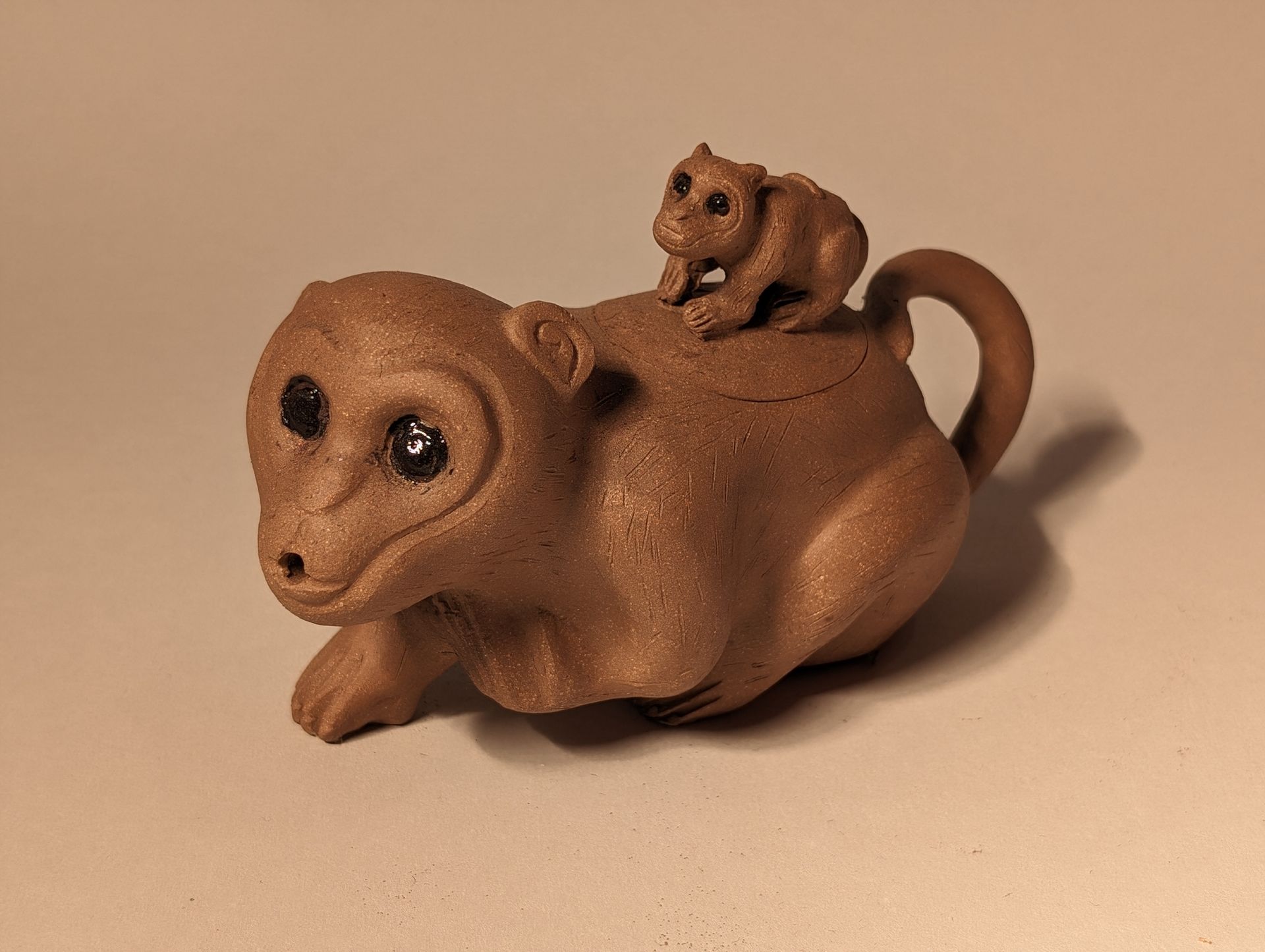 Brown ceramic animal figurine with a tiny cat riding on its back, against a plain beige background