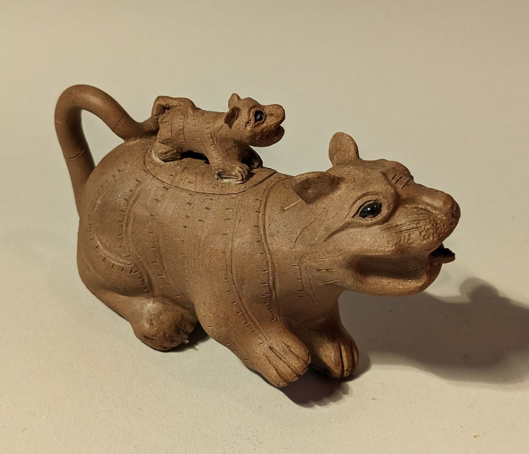Wooden figurines of a dog with a cat riding on its back on a plain background