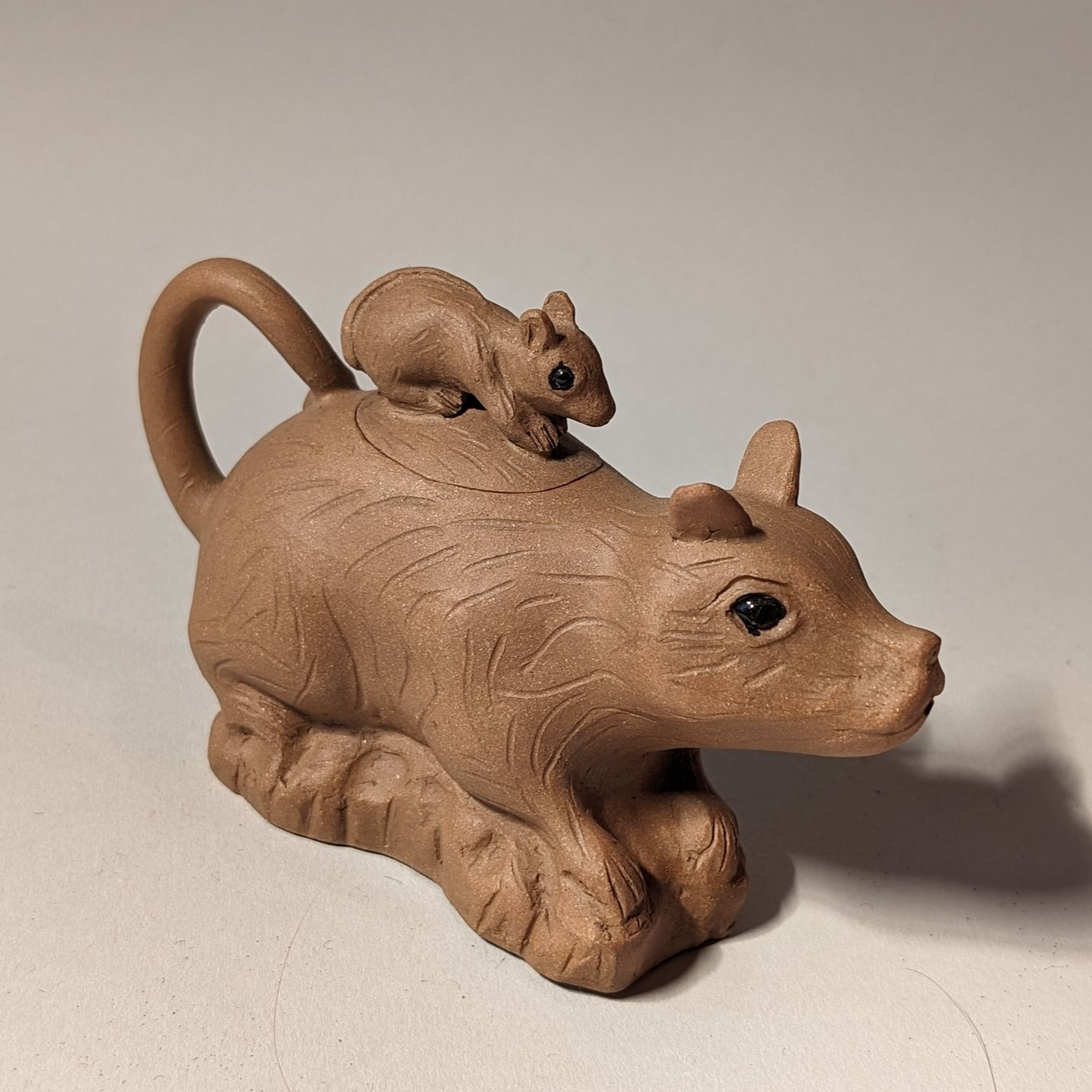 Wooden mouse figurine with a smaller mouse on its back, on a plain background