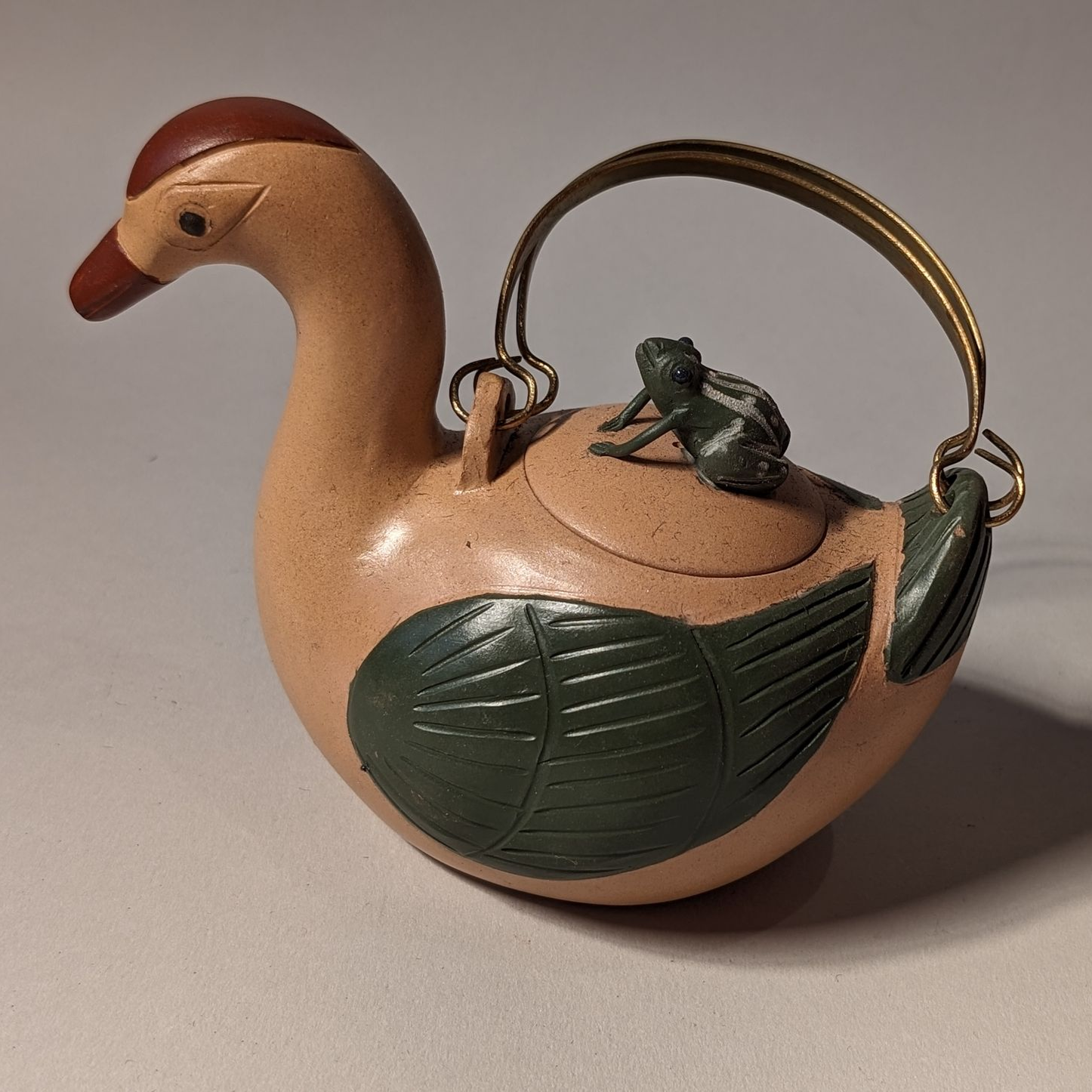 Teapot shaped like a bird with tan body, green leaf details, and a curved handle