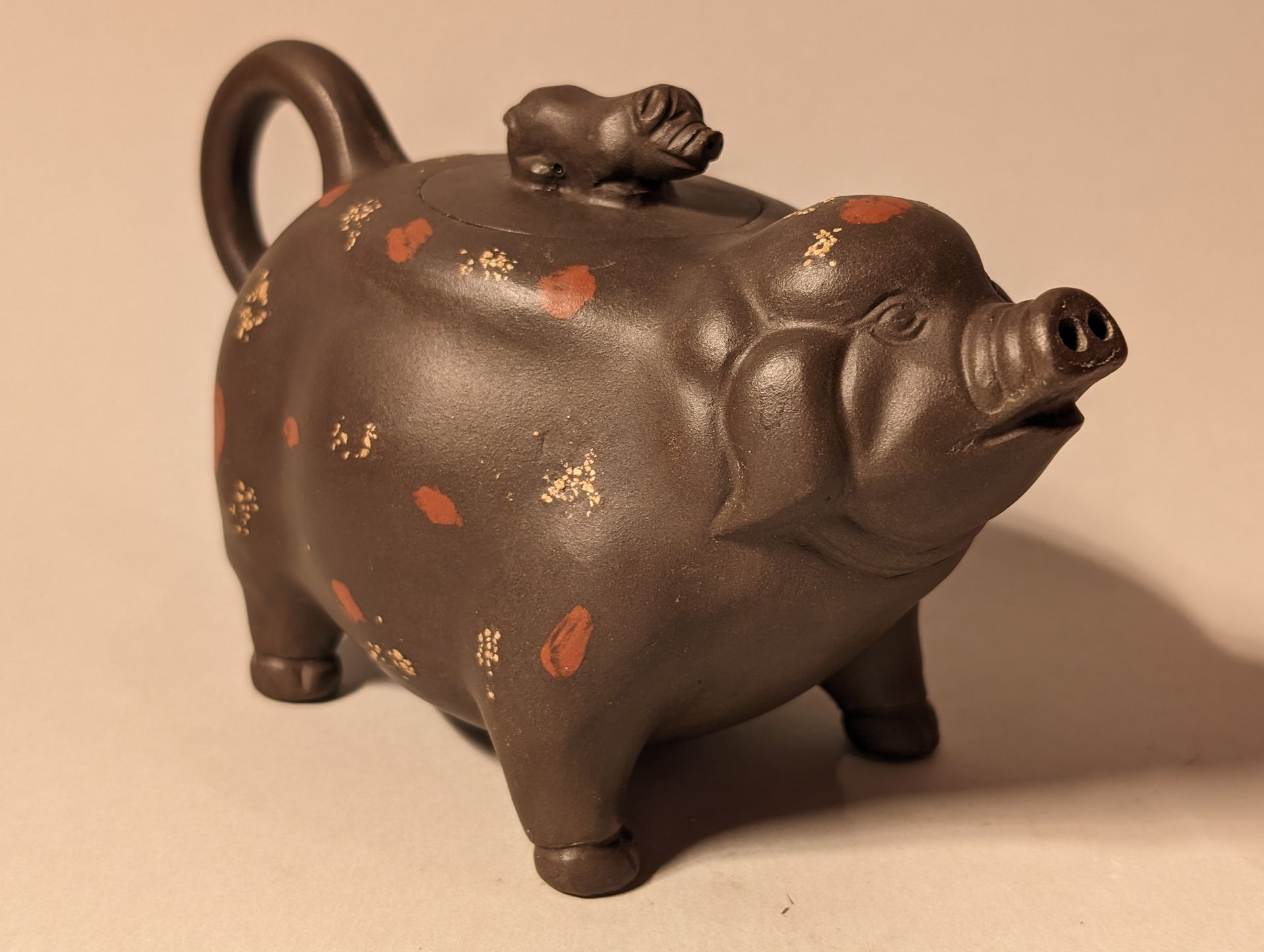 Brown ceramic pig teapot with painted floral accents on a light background