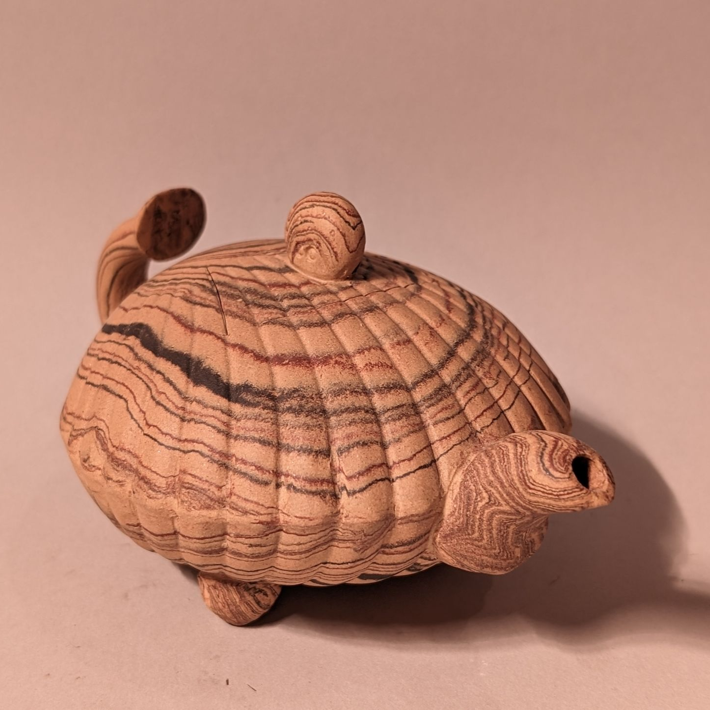 Hand-carved wooden turtle with striped shell and curled head and tail on a plain background