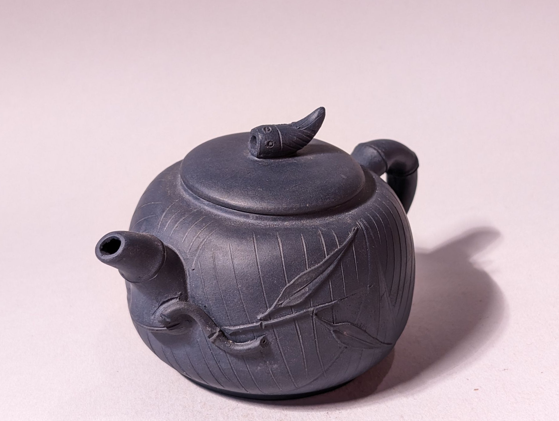 Dark gray teapot with a leafy vine design and curved spout on a light background
