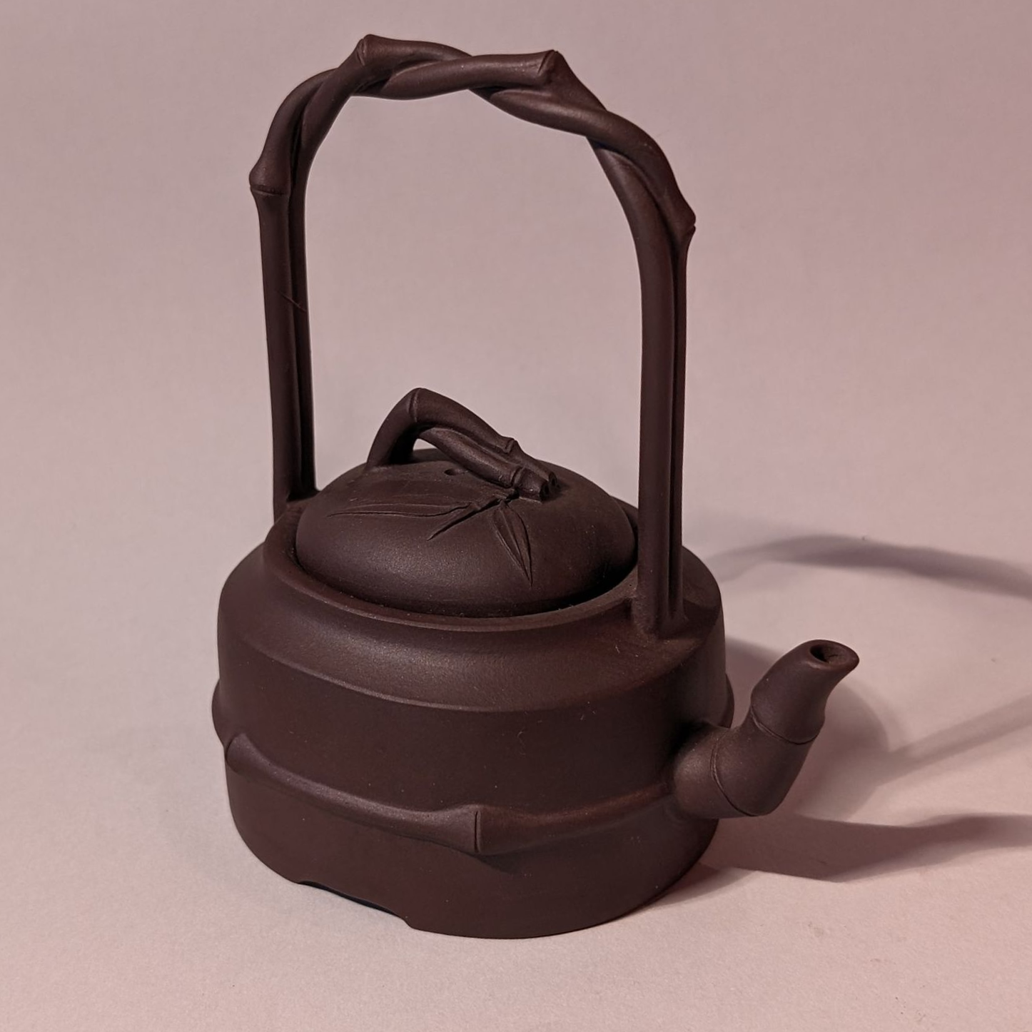 Dark brown cast iron teapot with woven handle and spout on a plain background