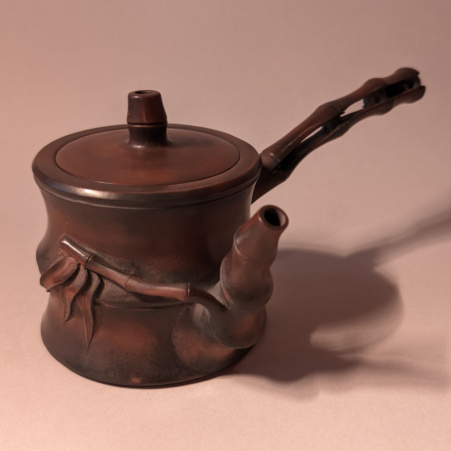 Brown ceramic teapot with lid and curved handle on a pink background