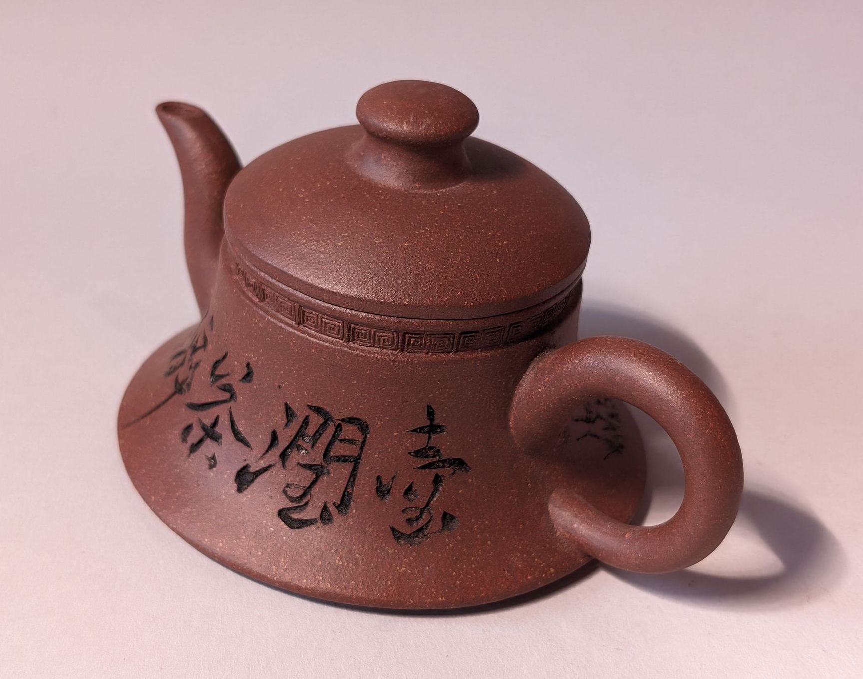 Brown clay teapot with black calligraphy on the side, shown on a plain light background