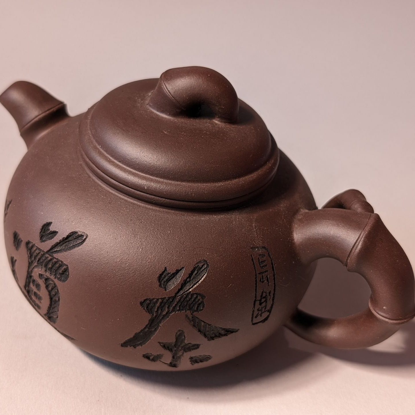 Brown clay teapot with black floral designs on a light background