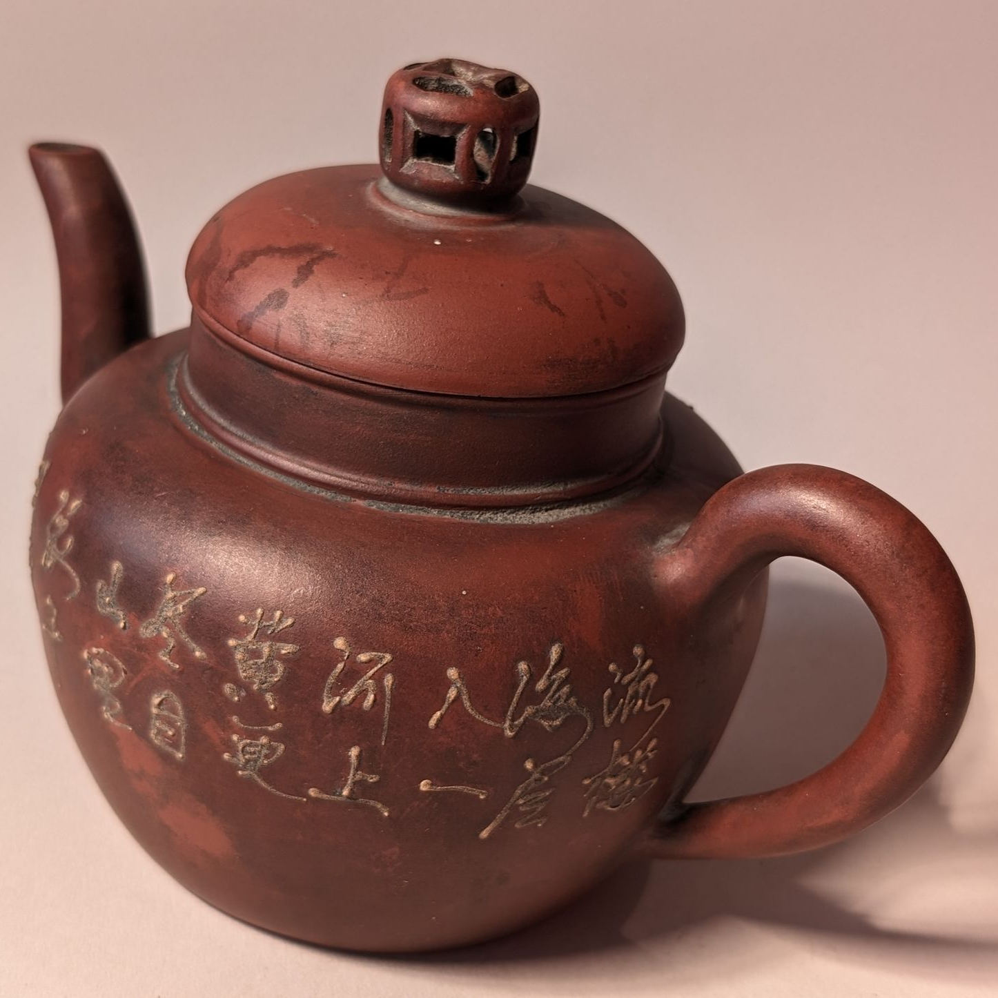 Brown ceramic teapot with a lid and handle, engraved with Chinese characters, on a plain background