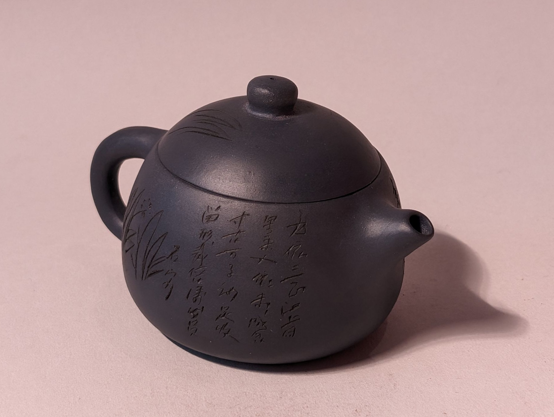 Black teapot with lid and handle, decorated with subtle patterns, on a light background