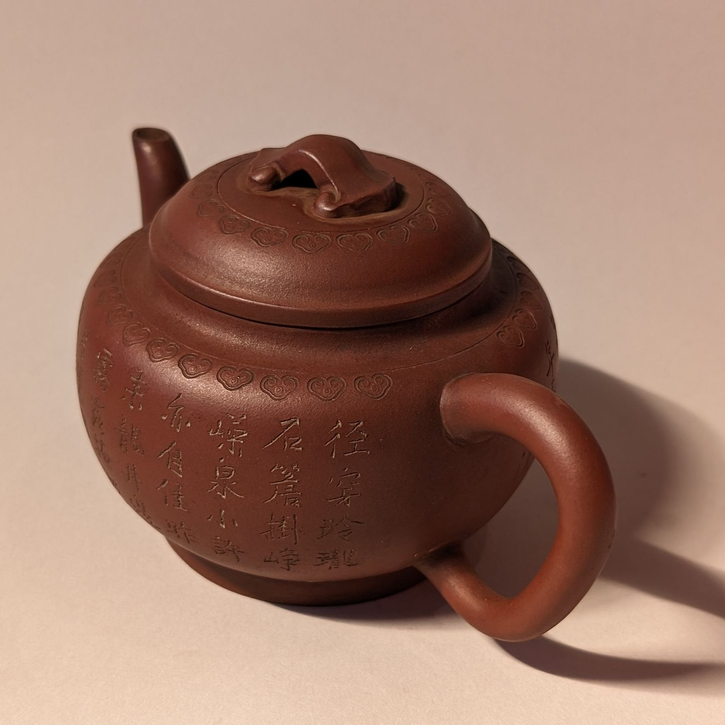 Small brown ceramic teapot with lid and handle on a plain background