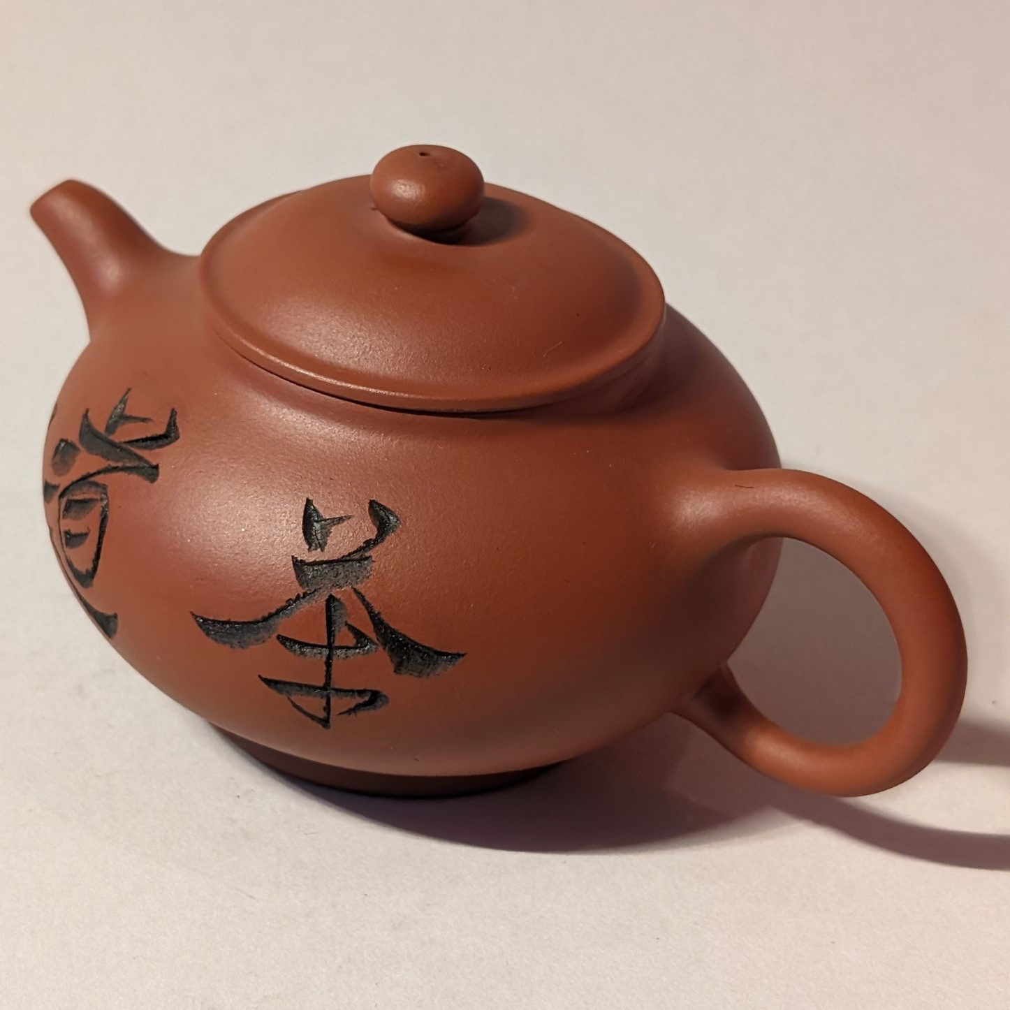 Brown ceramic teapot with black floral designs and a loop handle on a plain background