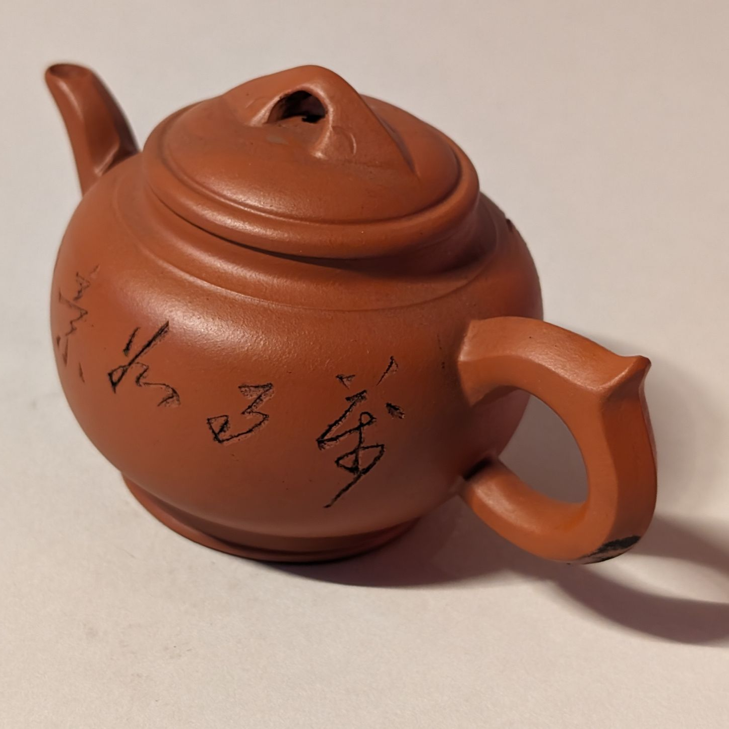 Brown clay teapot with black calligraphy on a plain background