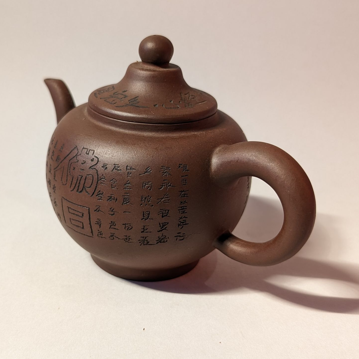 Brown ceramic teapot with Chinese characters, round body, loop handle, and lid on a white surface