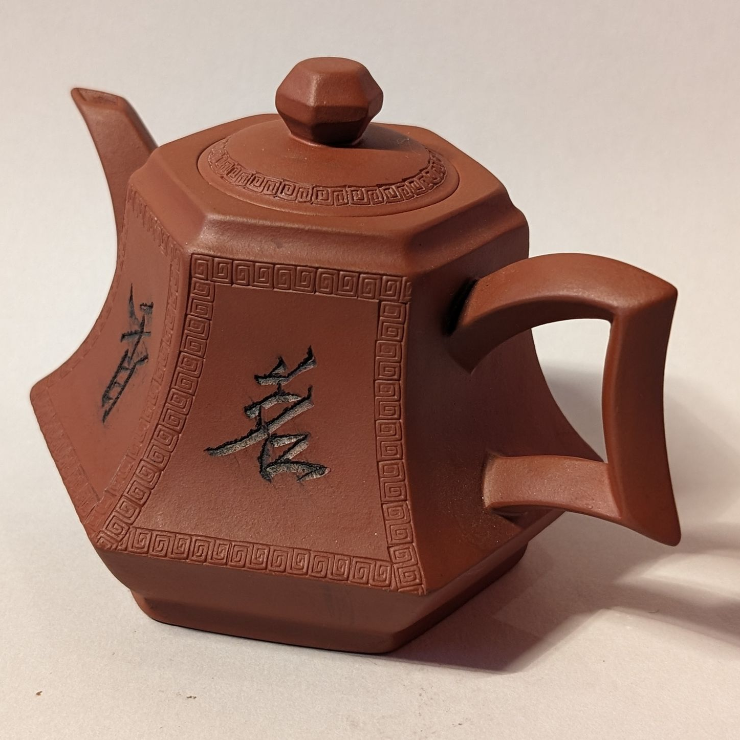 Brown hexagonal teapot with lid and handle, decorated with black characters on a plain light background