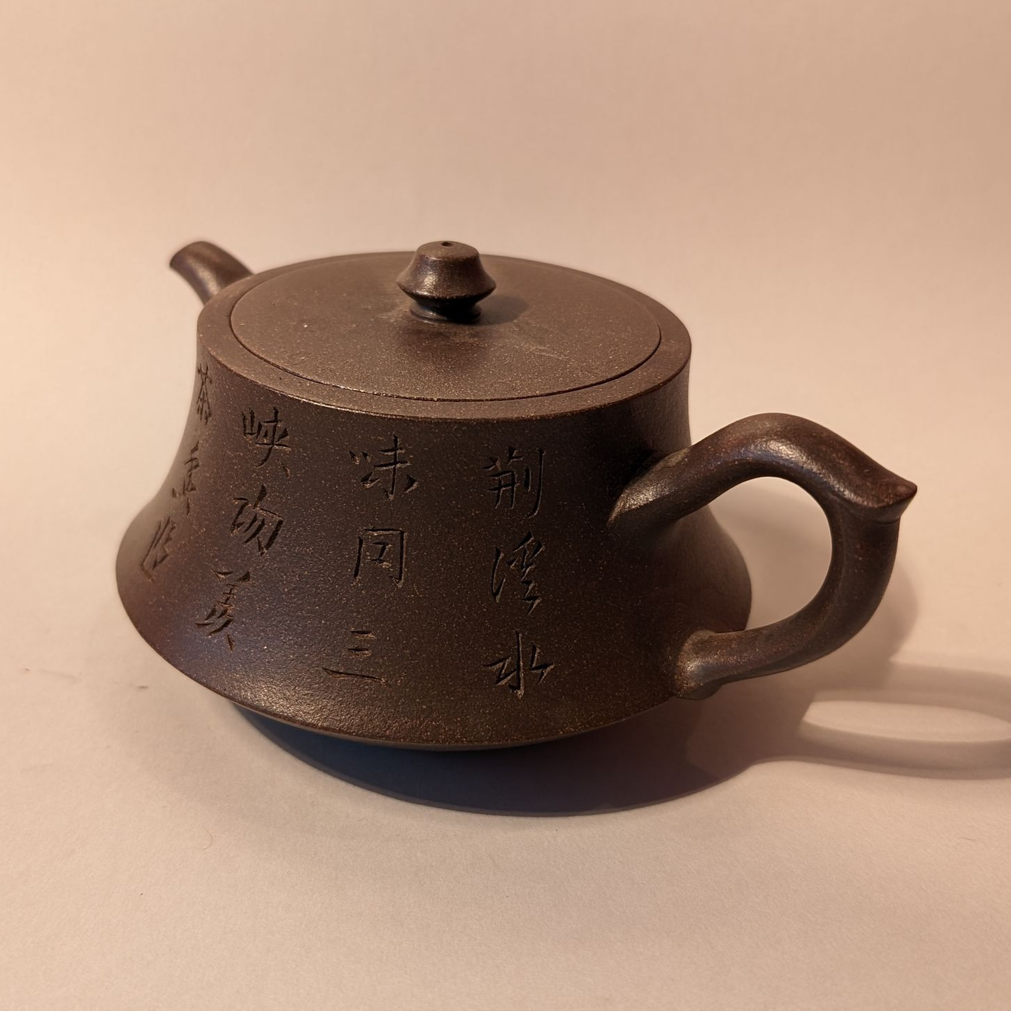 Small dark-brown cast-iron teapot with lid and side handle on a light surface
