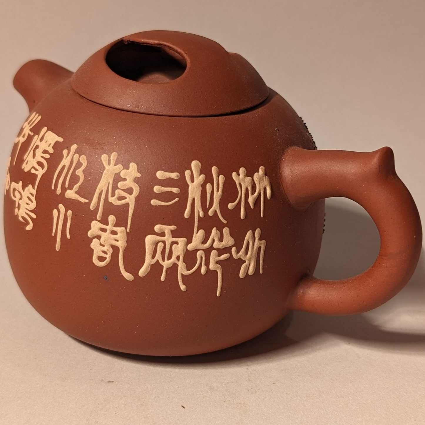 Brown clay teapot with a lid, handle, and white Chinese characters on the side