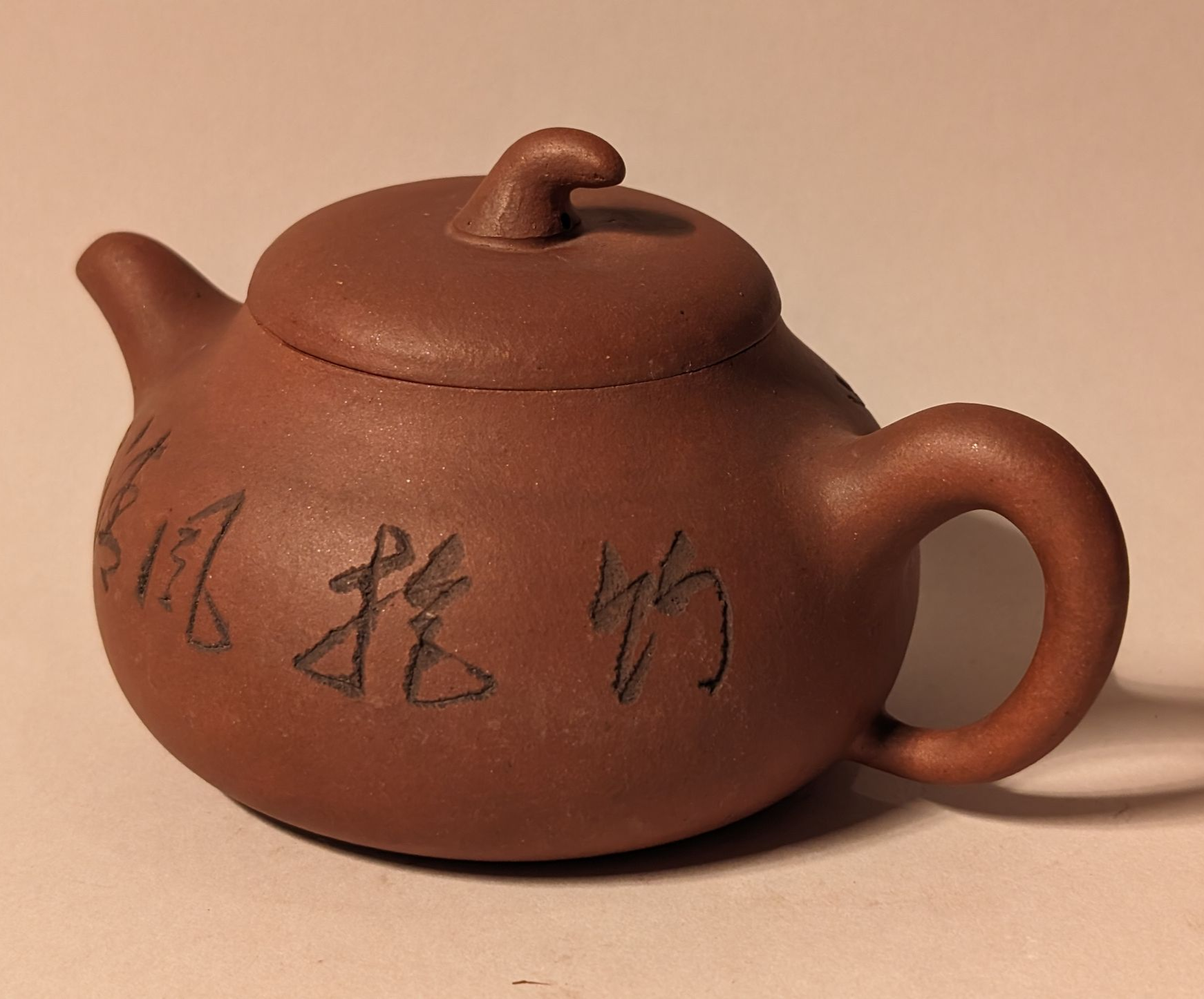 Brown ceramic teapot with Chinese characters on a beige background