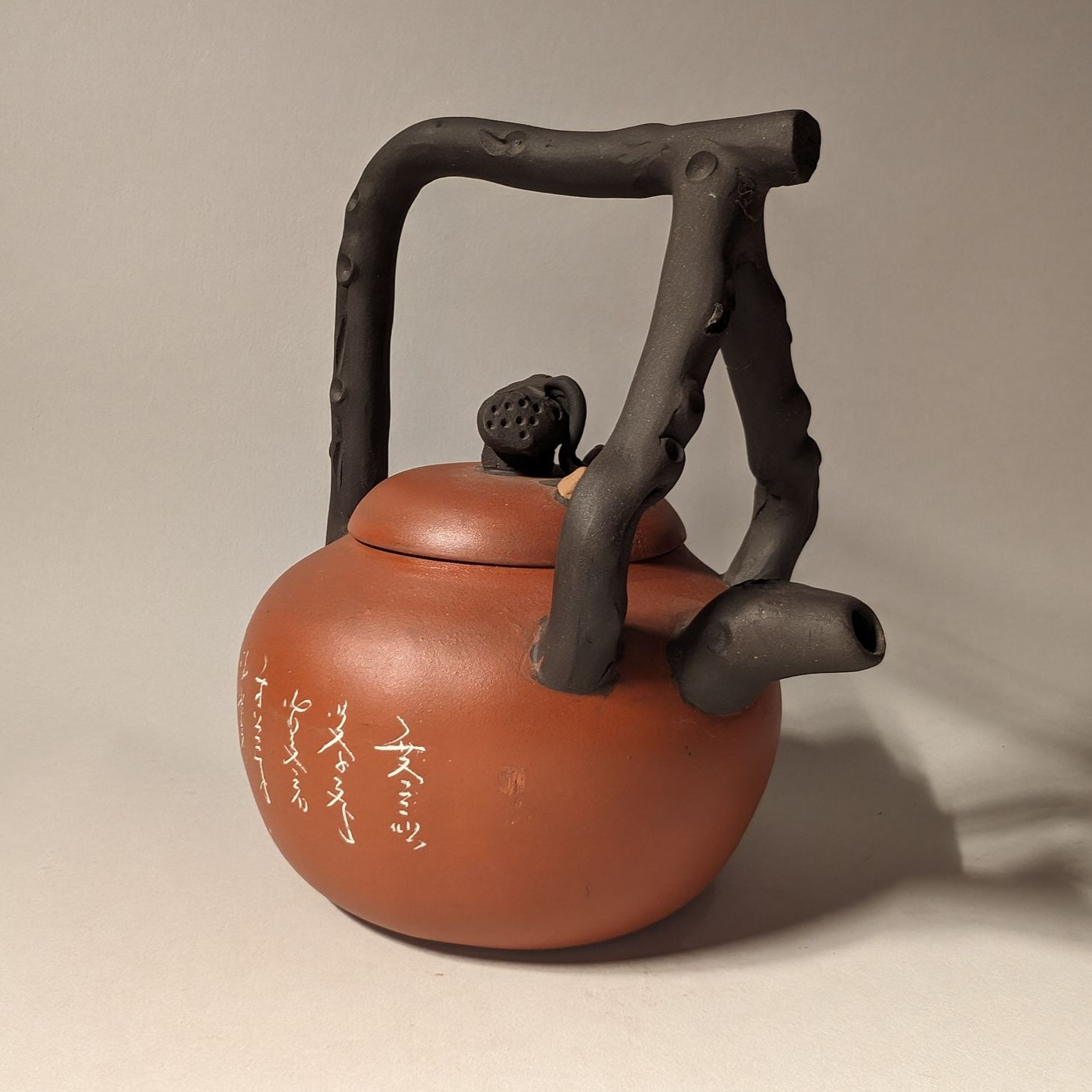 Small reddish-brown teapot with black handle and spout on a plain background