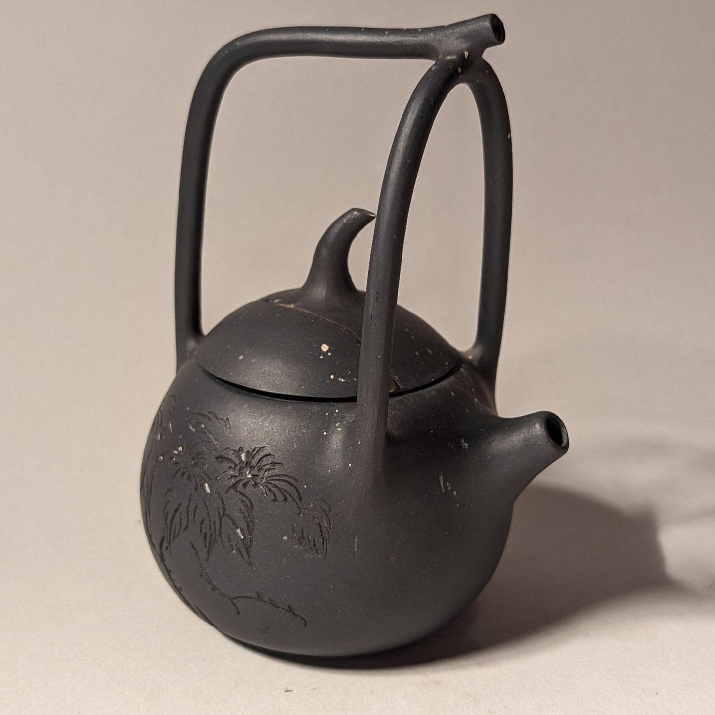 Black ceramic teapot with lid and tall handle on a plain surface