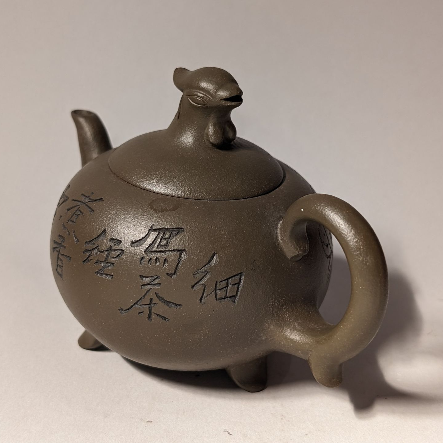 Small brown teapot with a cat-shaped lid and handle, decorated with Chinese characters.