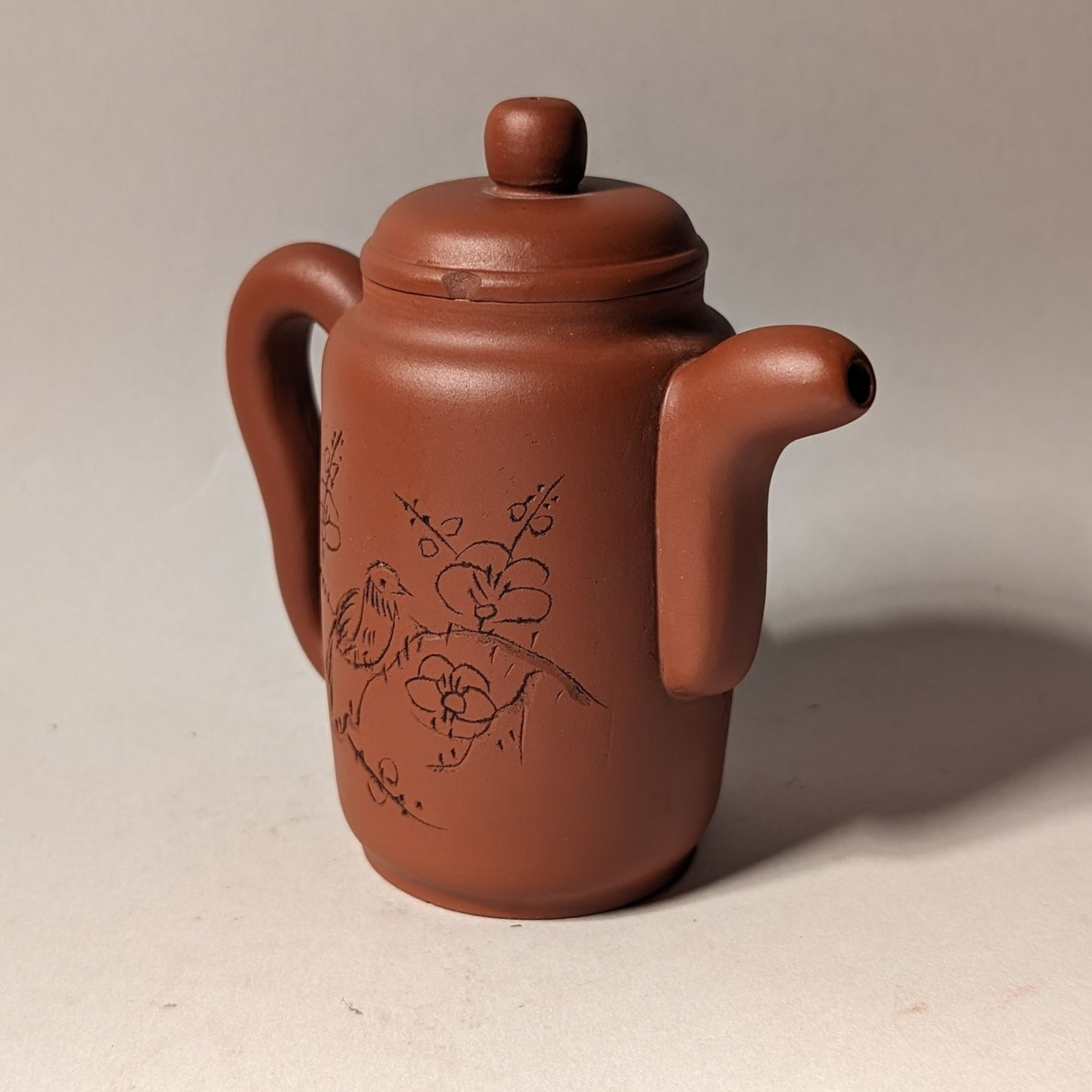 Small brown ceramic teapot with lid and floral decoration on a plain background