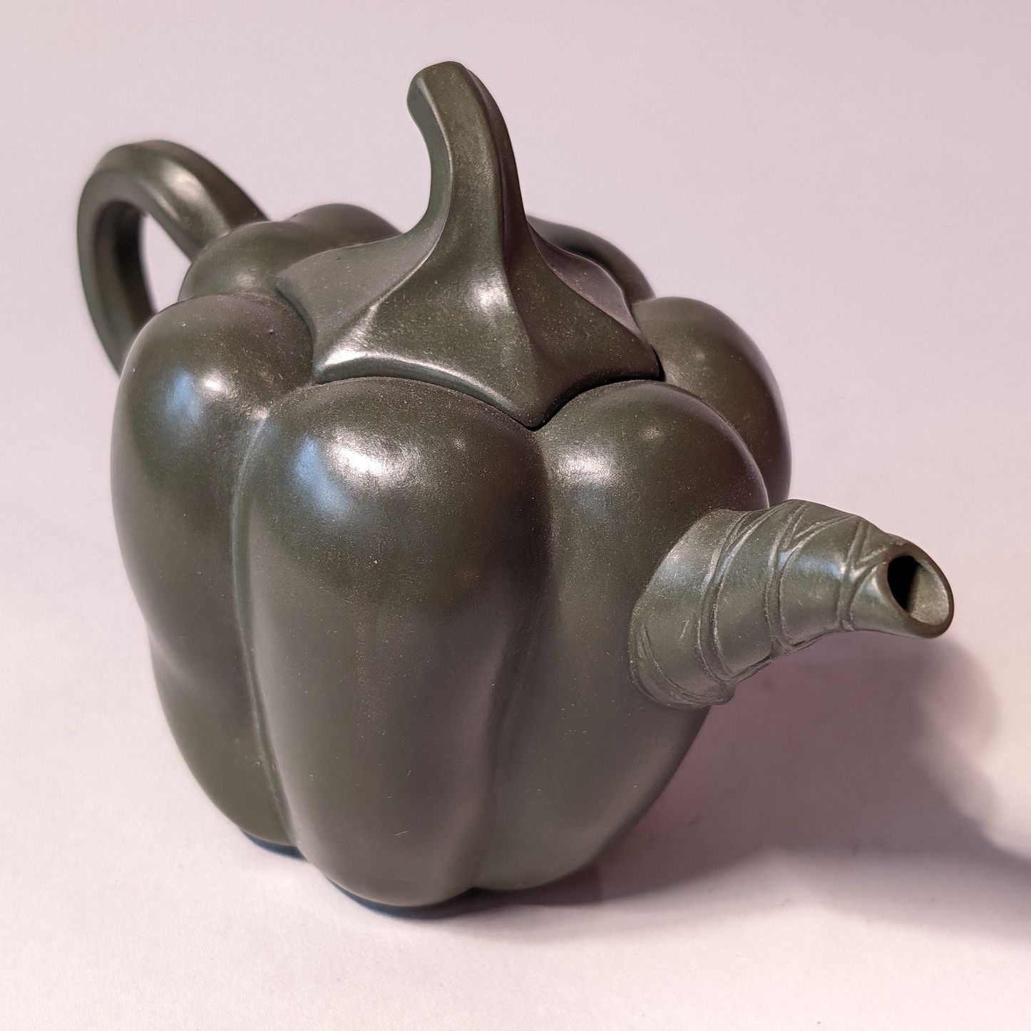 Metallic dark gray bell pepper-shaped teapot with a spout and handle on a light background
