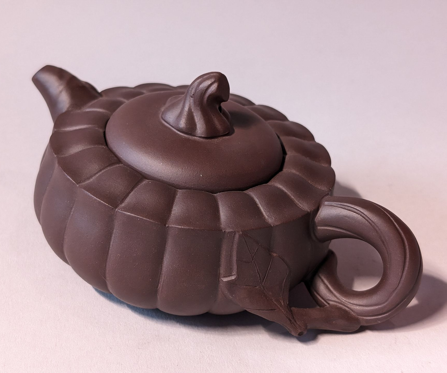 Dark brown ceramic teapot with a ribbed body, small spout, and loop handle on a light background