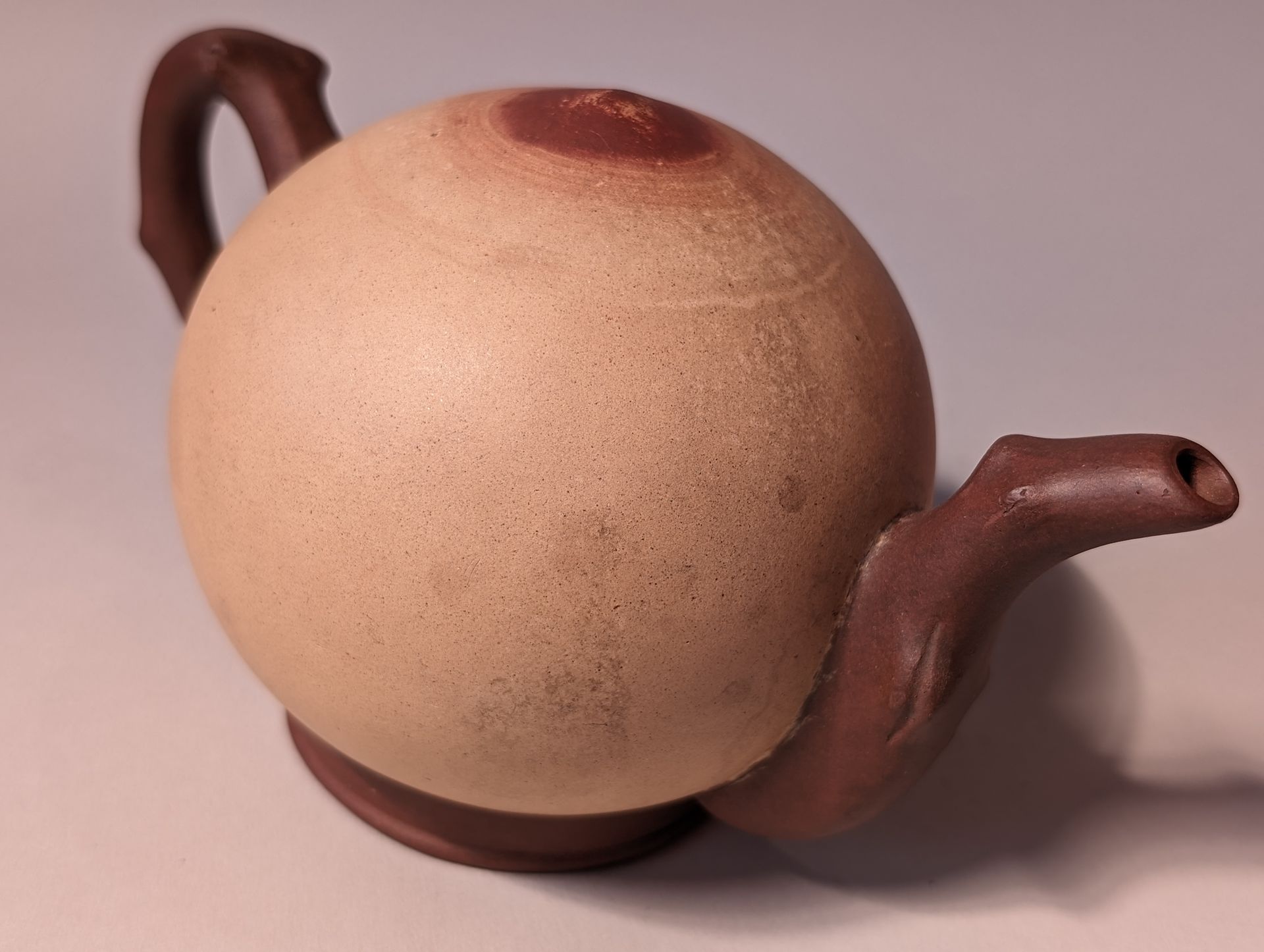 Brown teapot with a round body and curved spout on a light background