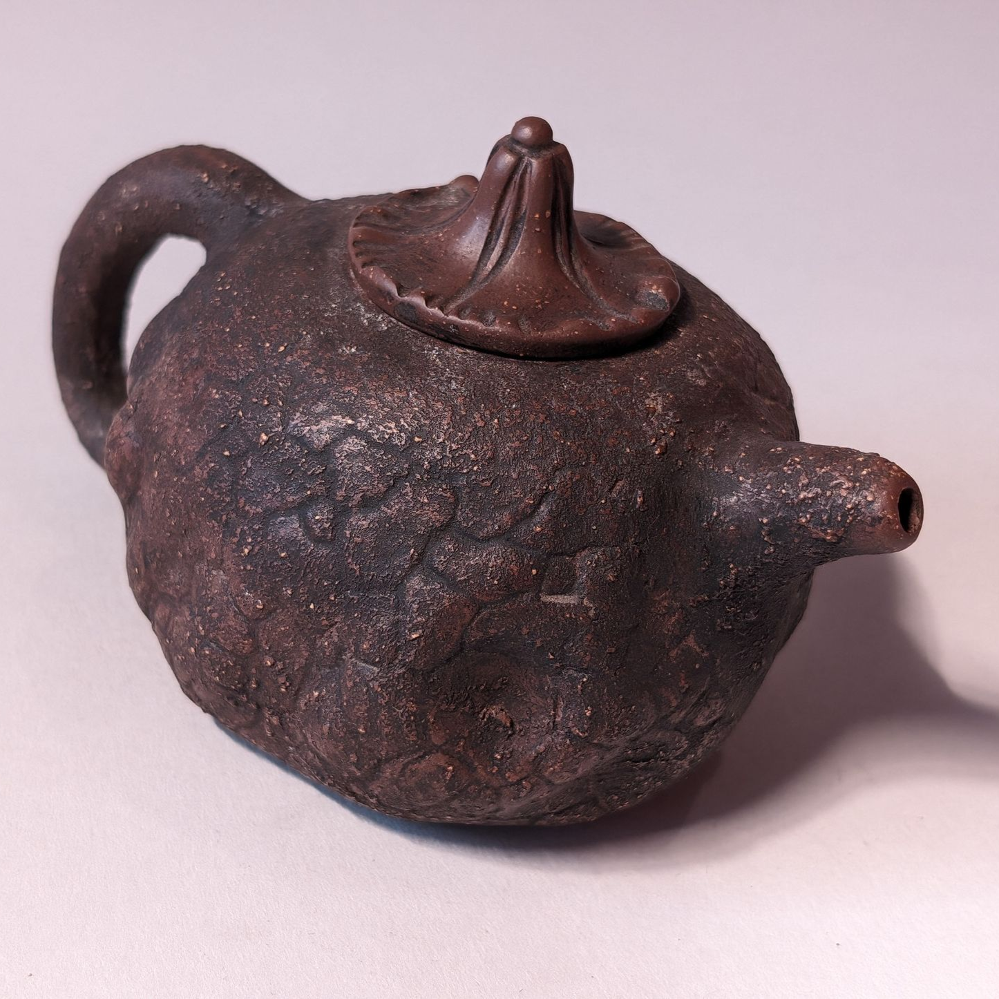 Small rustic brown teapot with a curved handle and pointed spout on a light background
