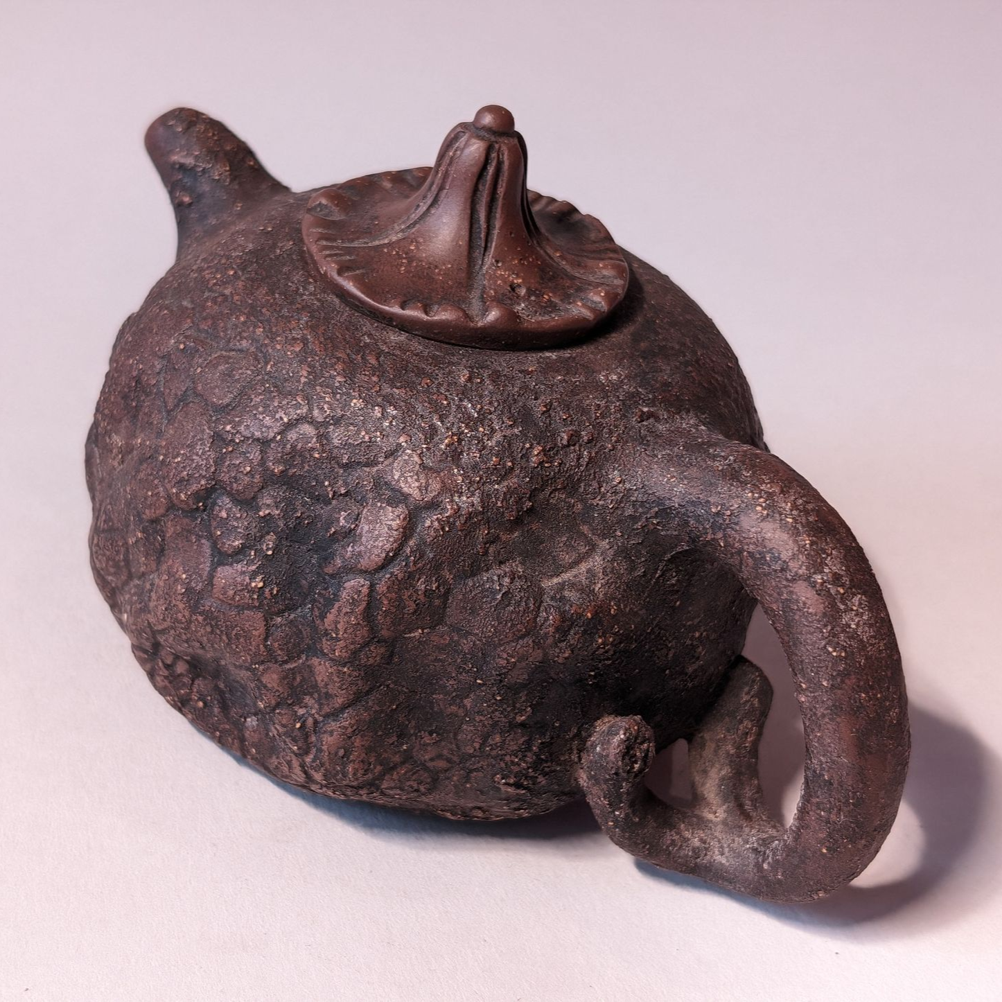 Brown cracked ceramic teapot with a curved spout and lid on a light background