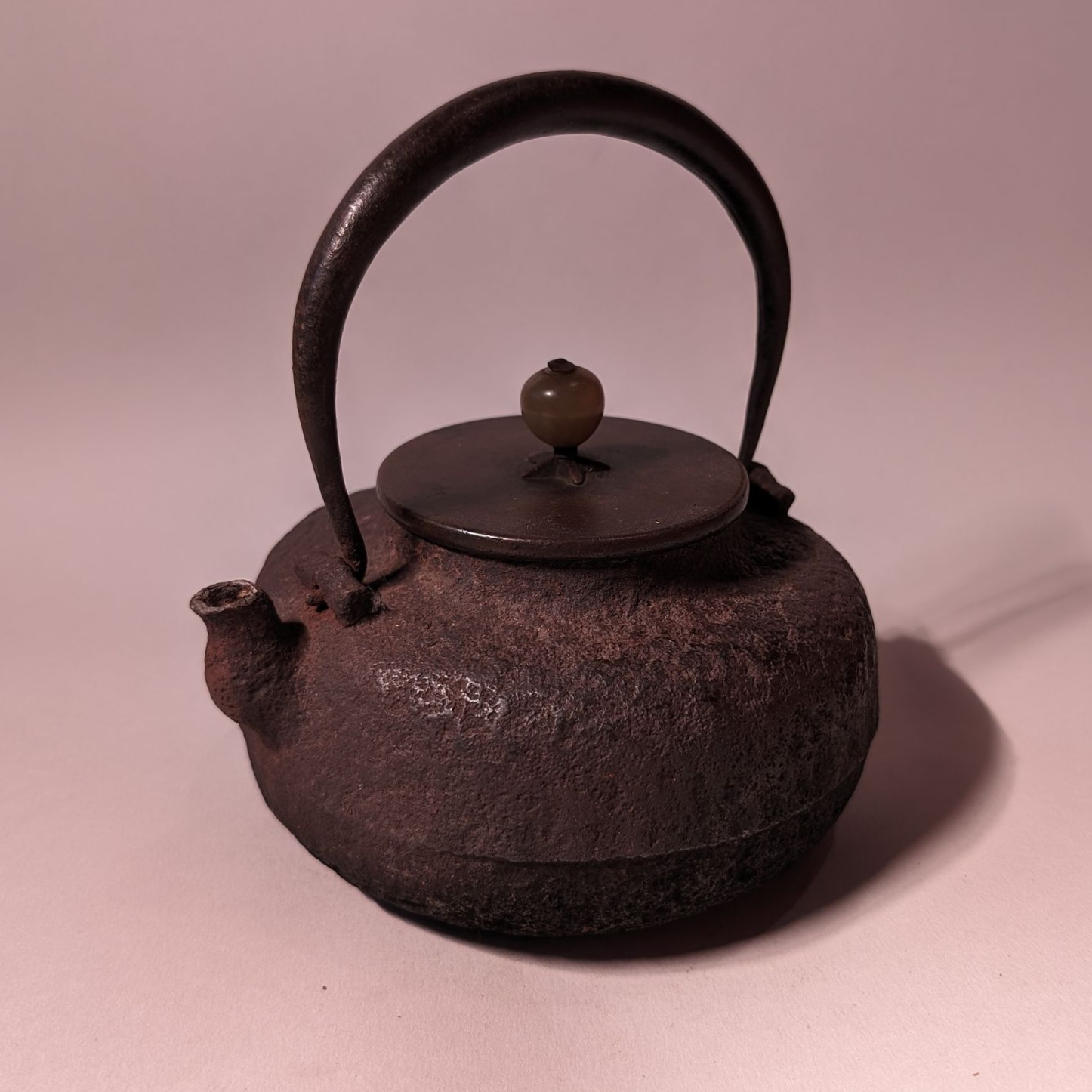 Rusty cast-iron teapot with arched handle and lid on a plain pink background