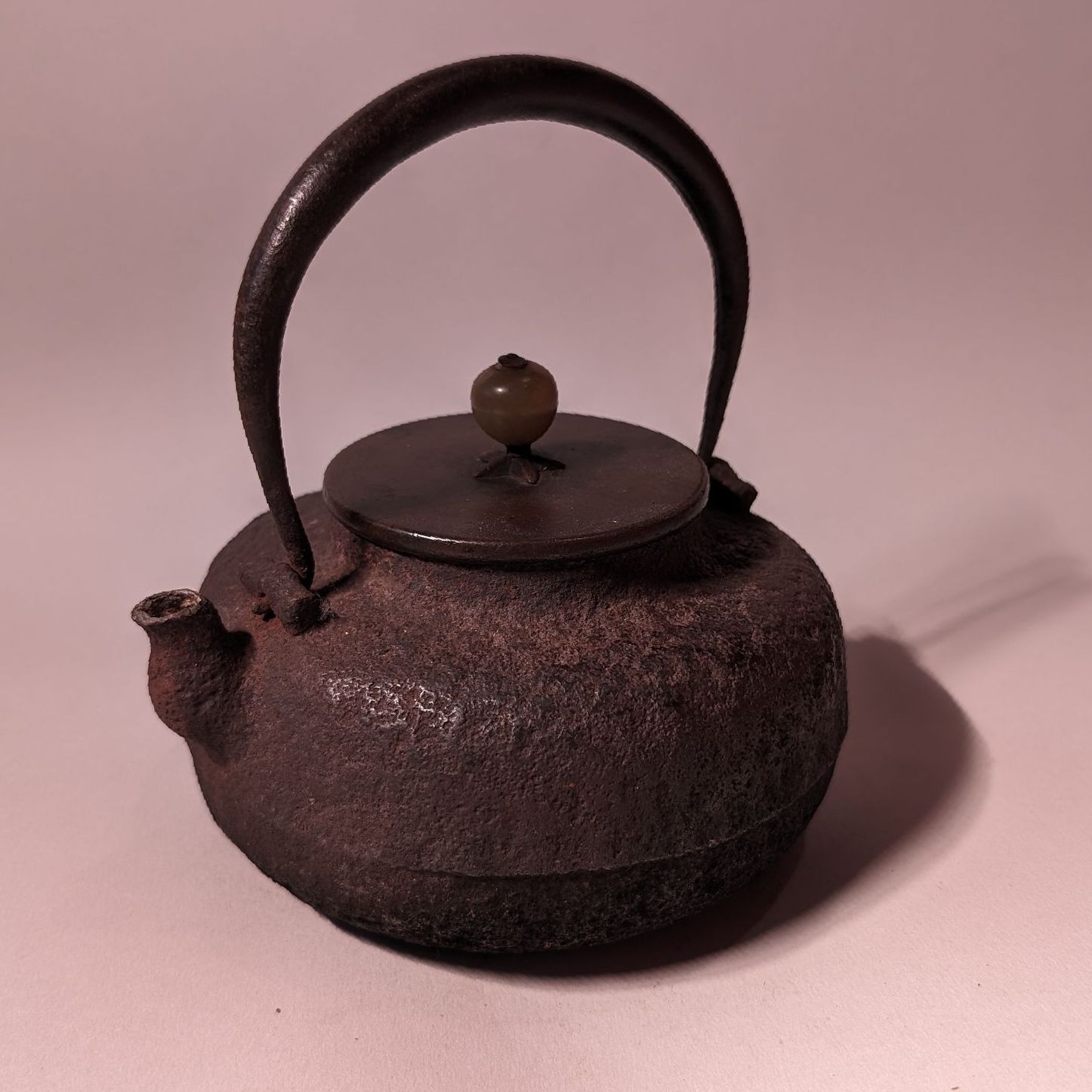 Small dark cast-iron teapot with arched handle and round lid on a pink background