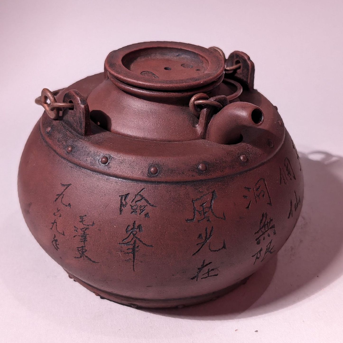 Small reddish-brown teapot with Chinese characters, round body, and lid on a pale background