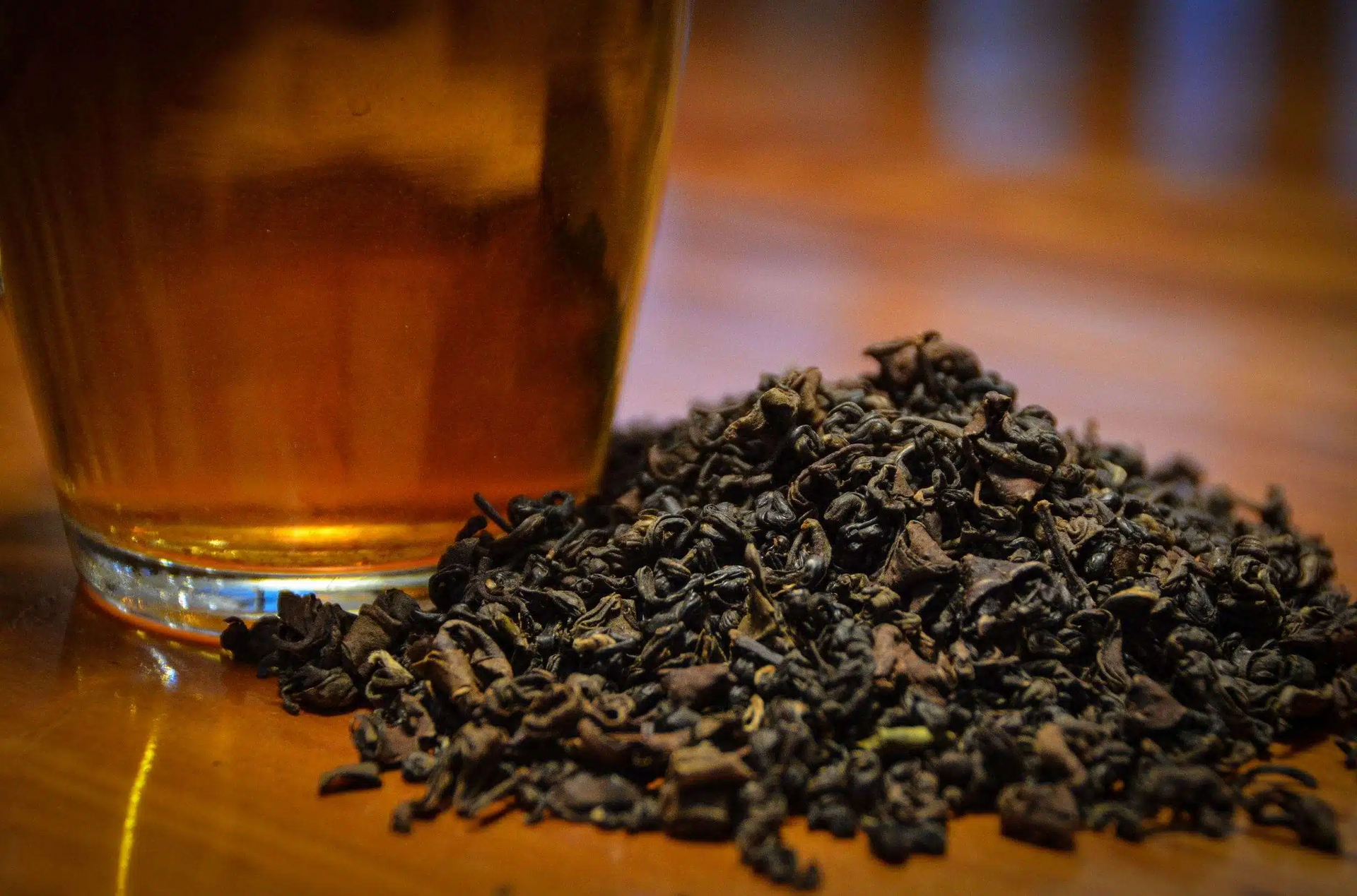 Glass of tea beside a pile of loose black tea leaves on a wooden table