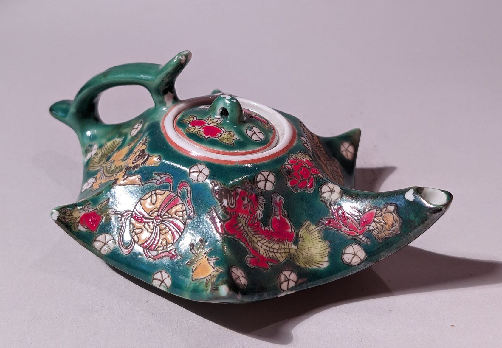 Decorative green teapot with floral patterns and red accents on a plain background