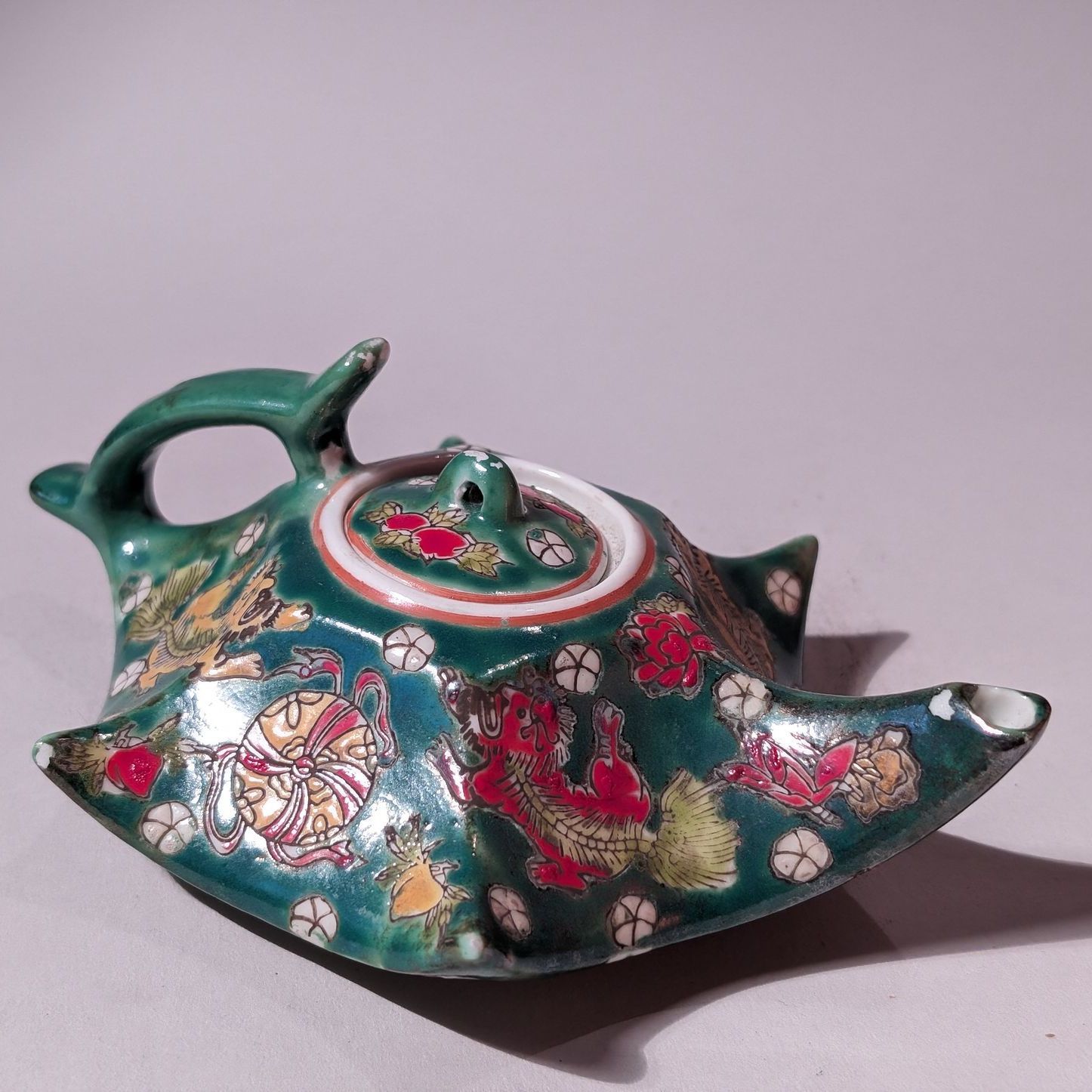 Decorative green jeweled teapot with floral and gold accents on a plain background